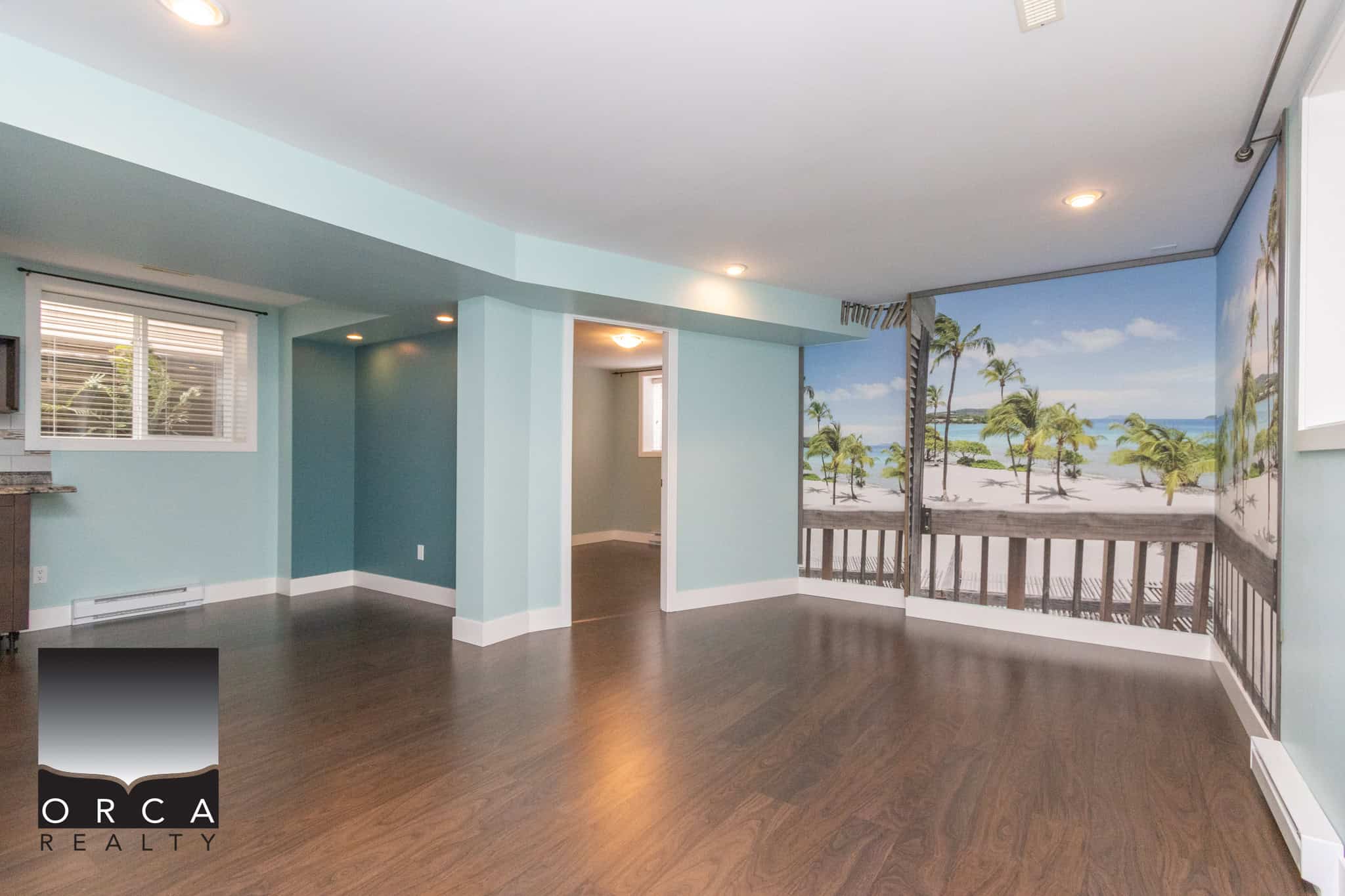 Spacious living room with beach-themed mural, hardwood floors, and large window, ideal for Vancouver Island real estate buyers seeking waterfront view properties.
