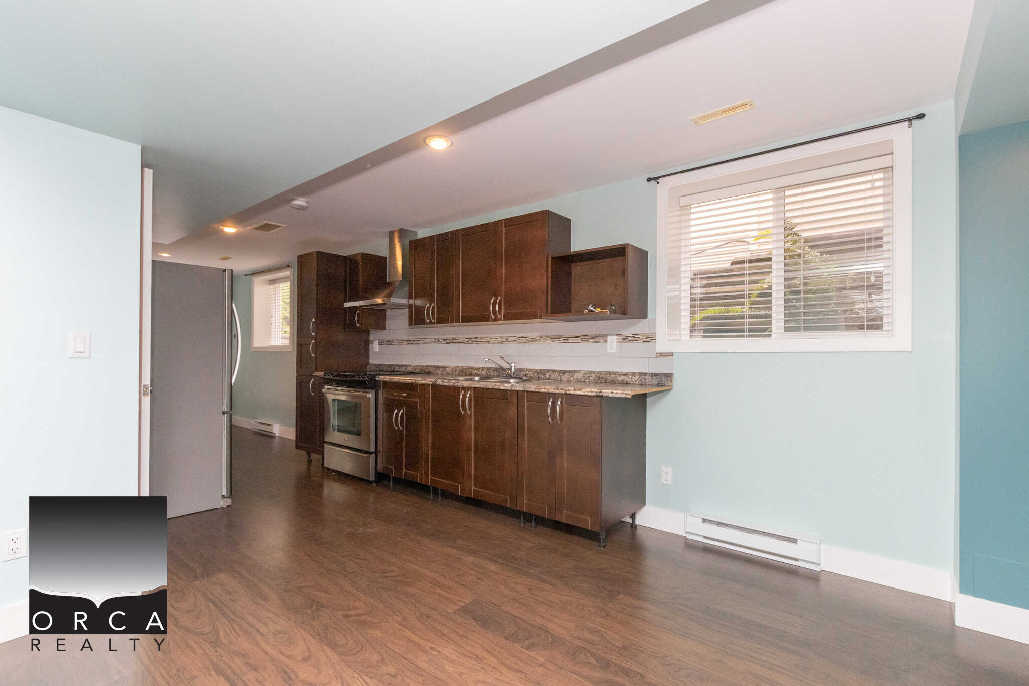 Bright modern kitchen with dark wood cabinetry, stainless steel stove, granite countertops, and natural light from large window – ideal for Vancouver Island homebuyers.