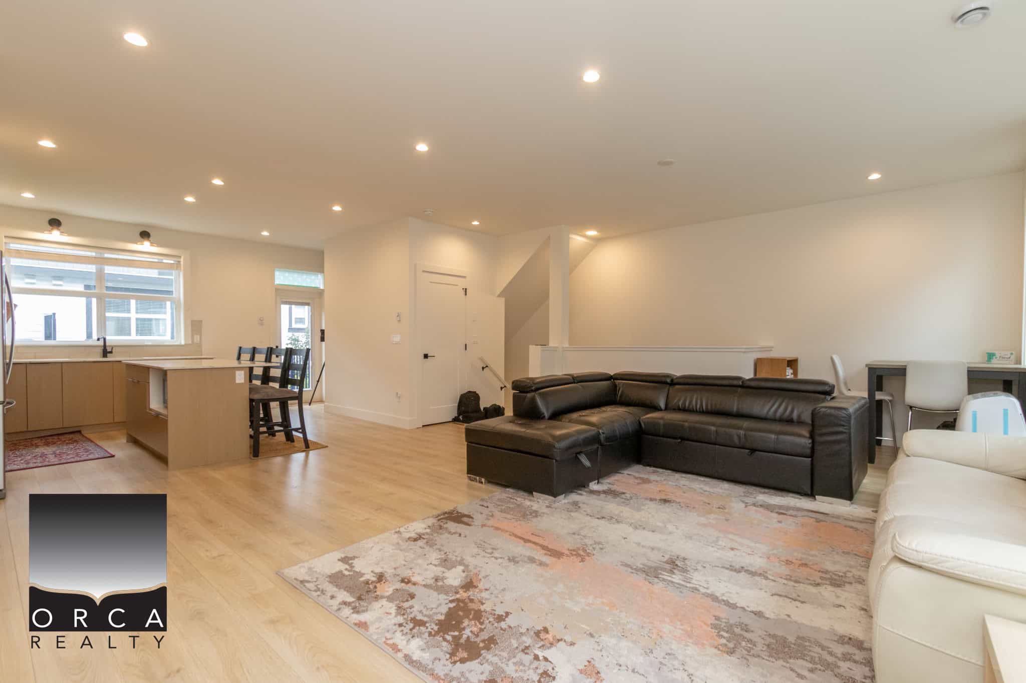 Spacious modern living room with open concept kitchen, stylish black leather sectional, bright natural light, and contemporary decor, ideal for family gatherings and entertaining.