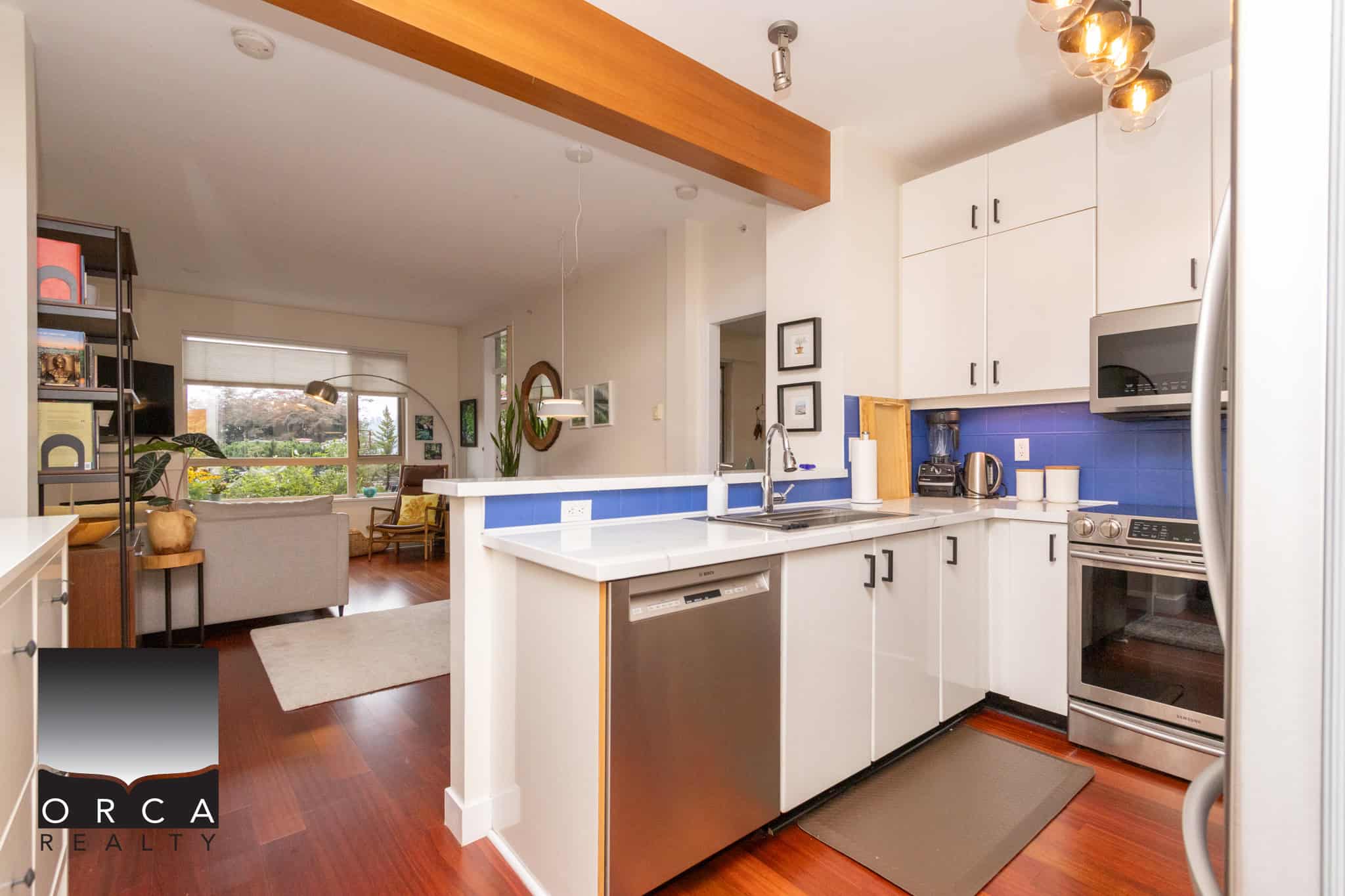 Bright modern kitchen with white cabinets, stainless steel appliances, vibrant blue backsplash, and hardwood flooring, connected to a stylish open-concept living area in a Vancouver home.