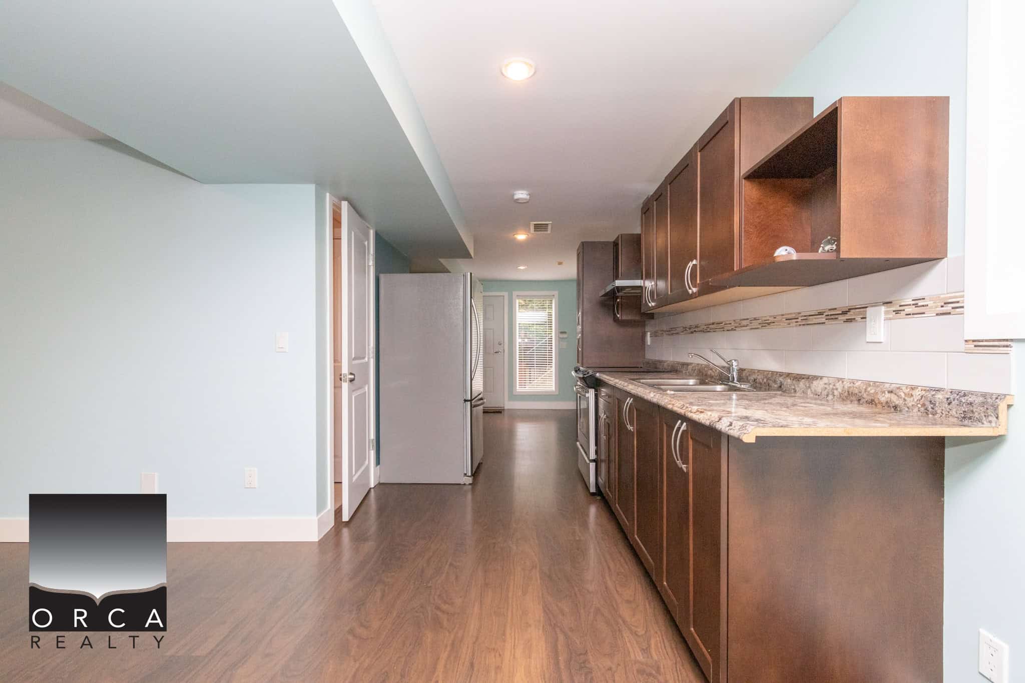 Bright modern kitchen with dark wood cabinets, granite countertops, stainless steel appliances, and light blue walls, perfect for homebuyers seeking contemporary Vancouver Island real estate.
