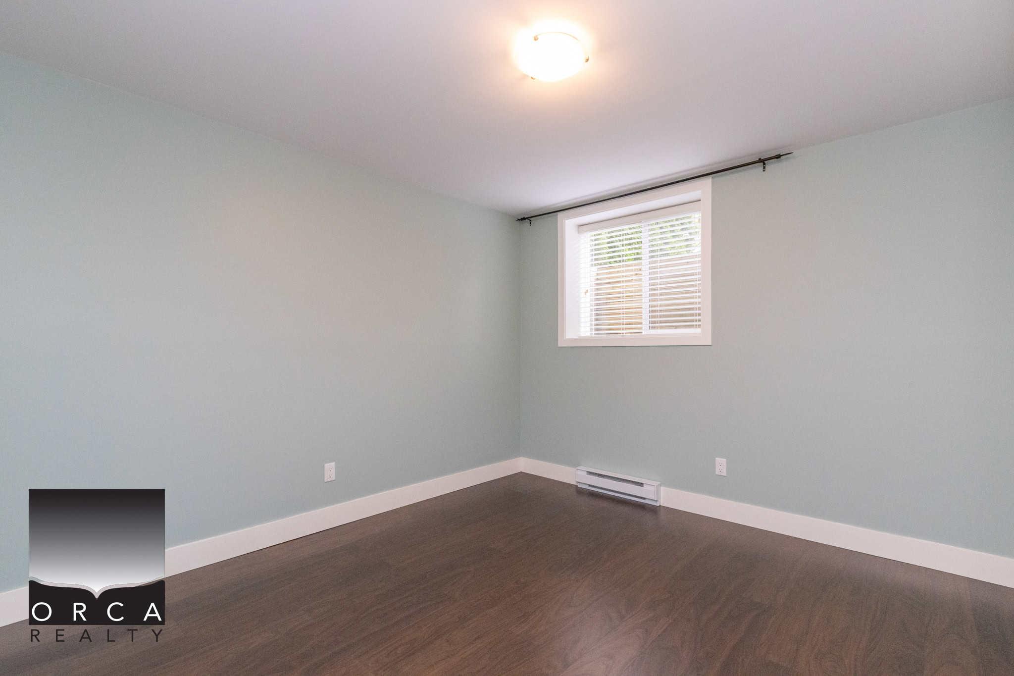 Bright empty bedroom with light green walls, hardwood flooring, and a window with blinds, showcasing a clean and modern interior ideal for Vancouver real estate listings.