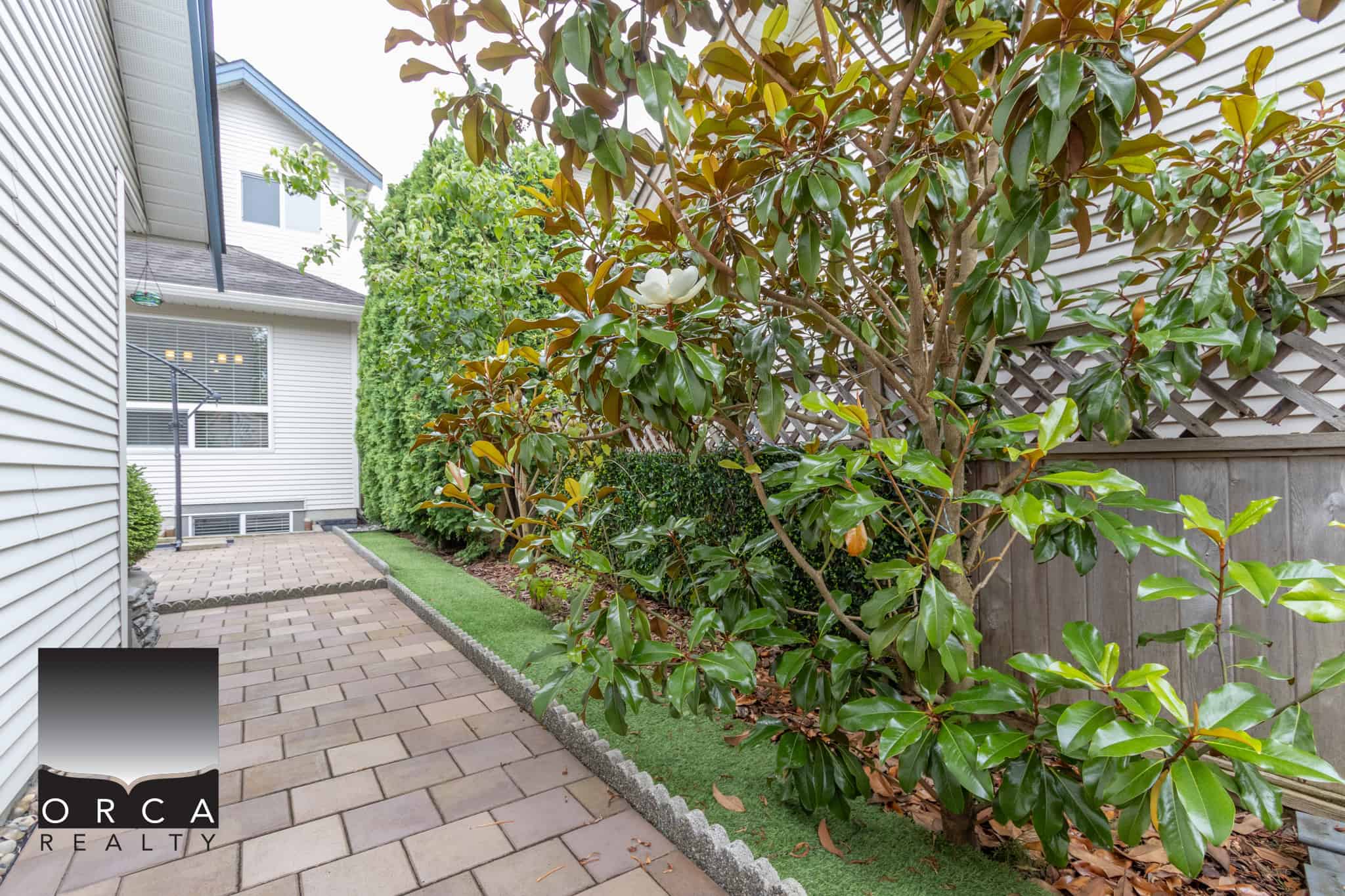 Lush landscaped backyard with mature greenery, paved walkway, and privacy fencing, ideal for outdoor living in Vancouver Island.