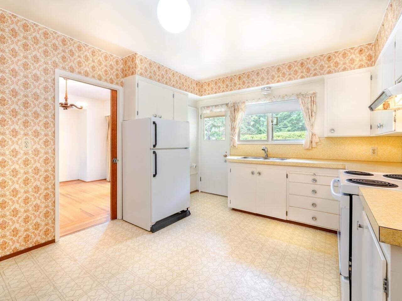 Updated kitchen with white cabinets, vintage wallpaper, and natural light in a charming home for sale by Orca Realty Inc. in the Vancouver area.