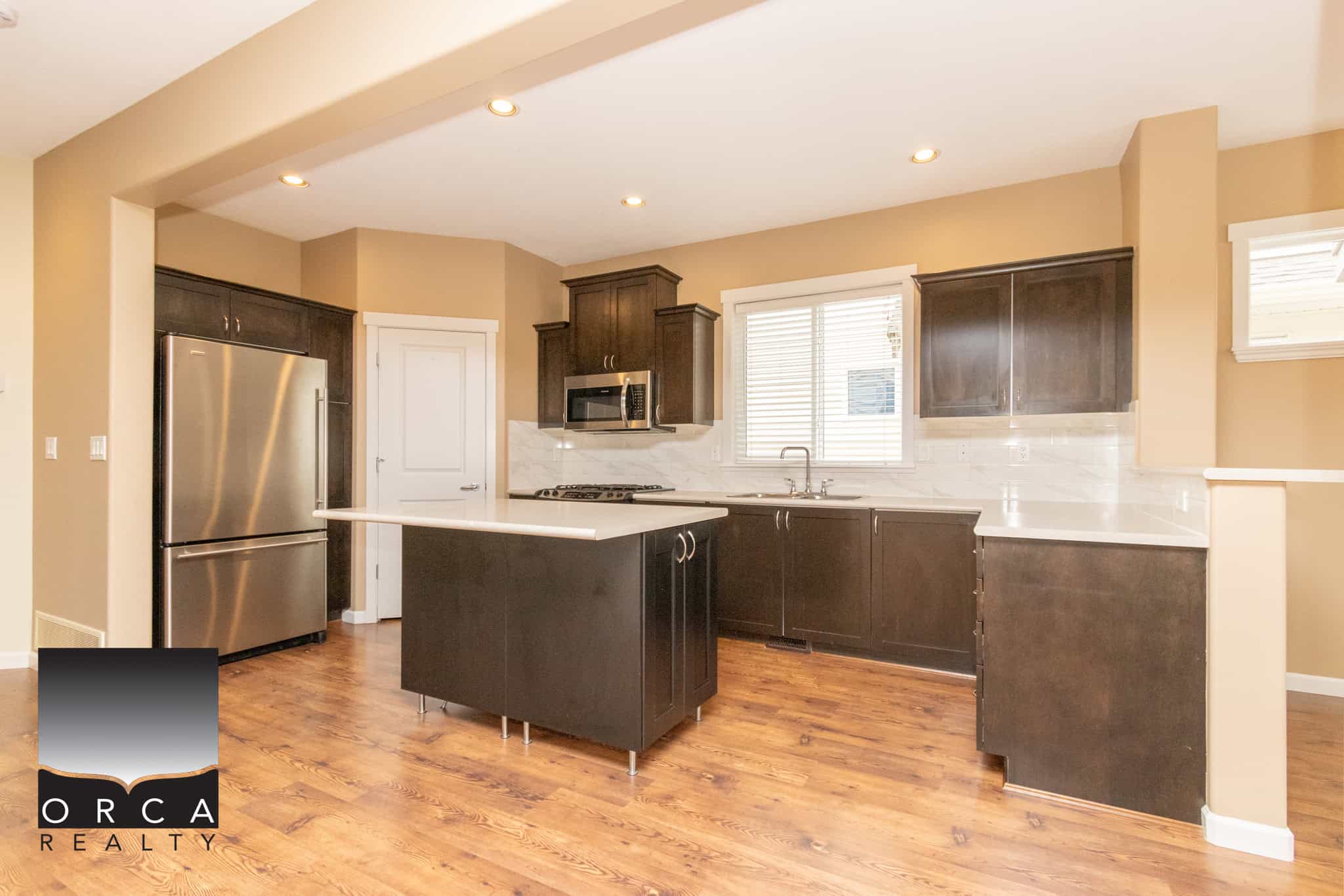Modern kitchen with stainless steel appliances and dark wood cabinetry, featuring a spacious island, hardwood flooring, and updated finishes, ideal for Vancouver homebuyers.