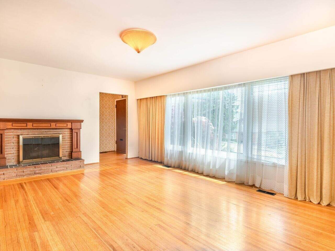 Spacious living room with large windows, hardwood flooring, and a cozy brick fireplace, ideal for family gatherings and modern home comfort.