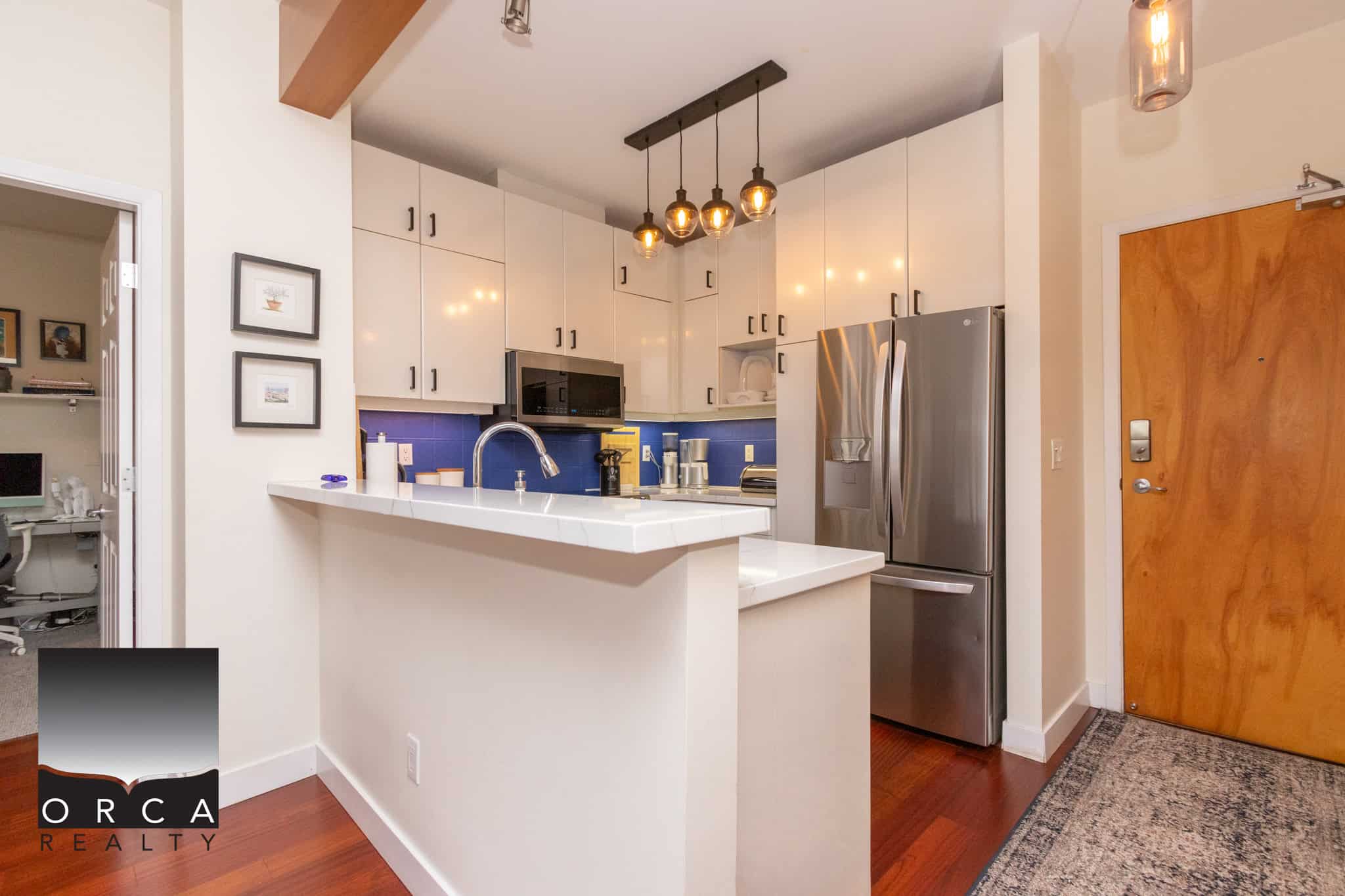Modern kitchen with white cabinetry, stainless steel refrigerator, blue backsplash, and stylish pendant lighting, showcasing Orca Realty Inc. expertise in Vancouver property sales and real estate services.