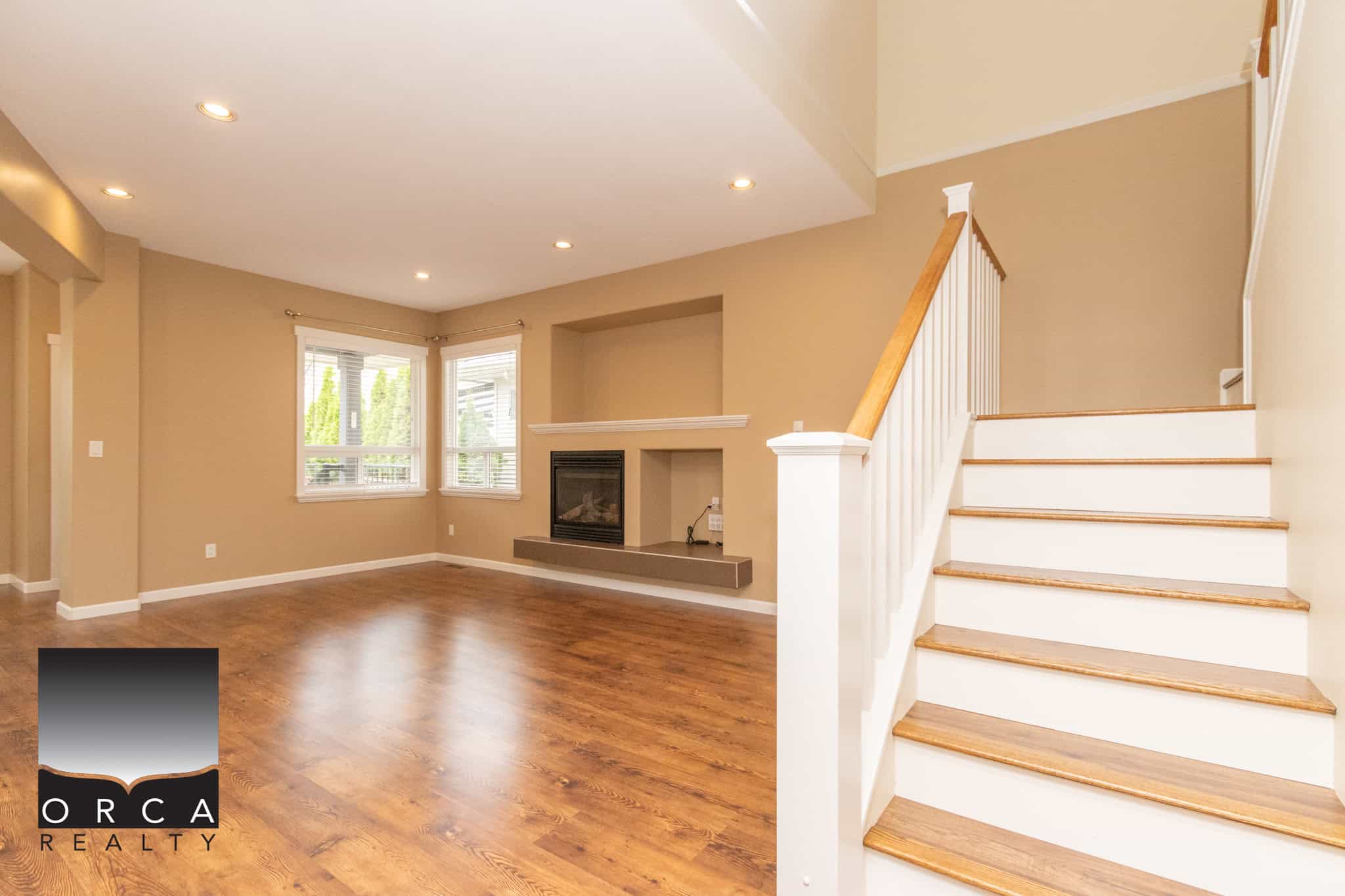 Spacious living room with hardwood floors, neutral wall colours, and a cozy fireplace, featuring large windows that bring in natural light, perfect for family living.