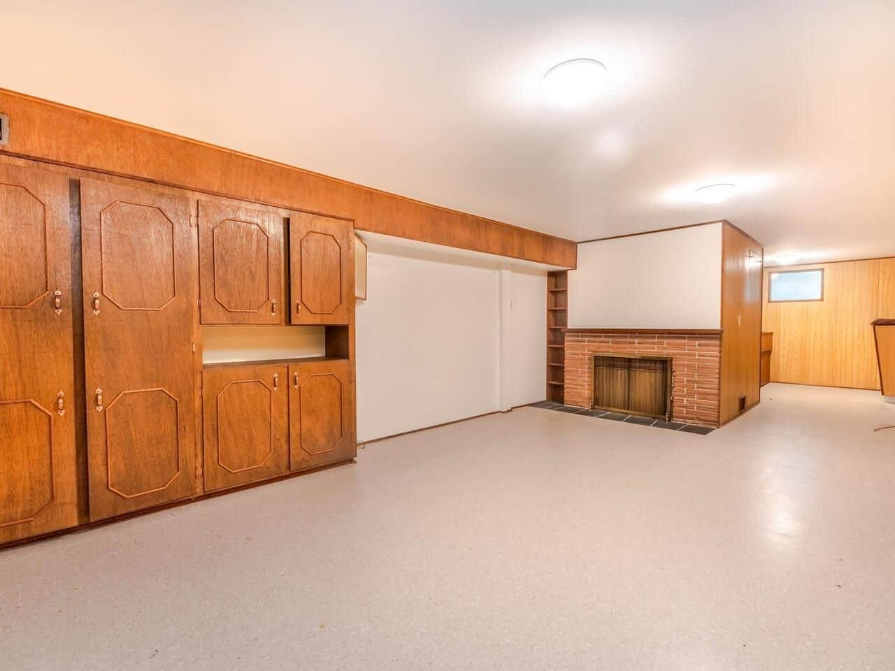 Spacious basement living area with built-in wooden cabinets and brick fireplace, ideal for family gatherings and relaxation in a well-maintained Vancouver home.