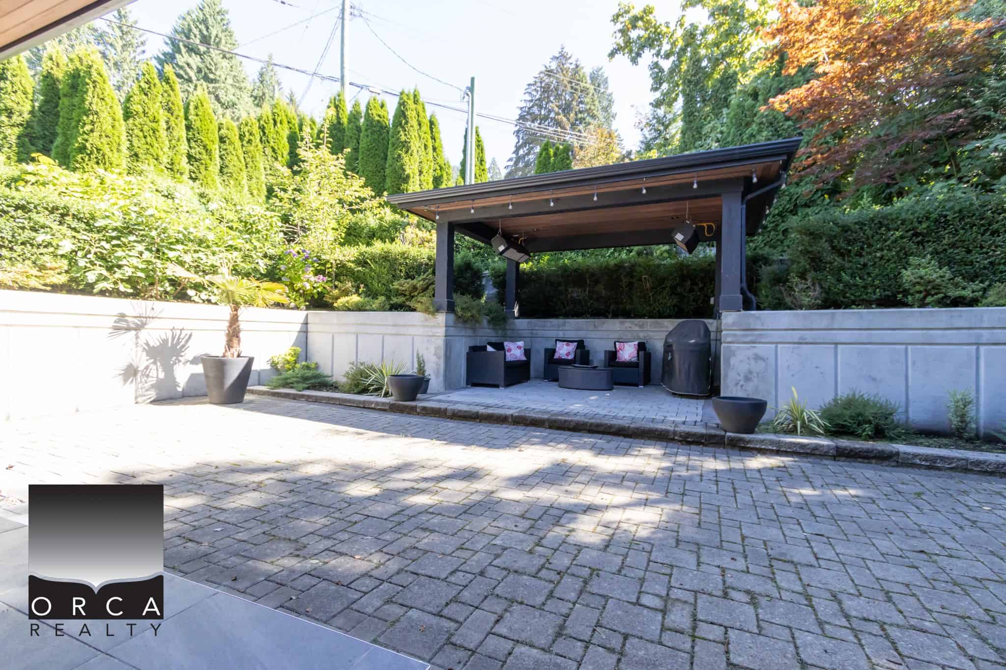 Spacious outdoor patio with a cozy shaded seating area, perfect for entertaining and relaxing in a beautiful, landscaped backyard. Ideal for outdoor gatherings and enjoying nature.