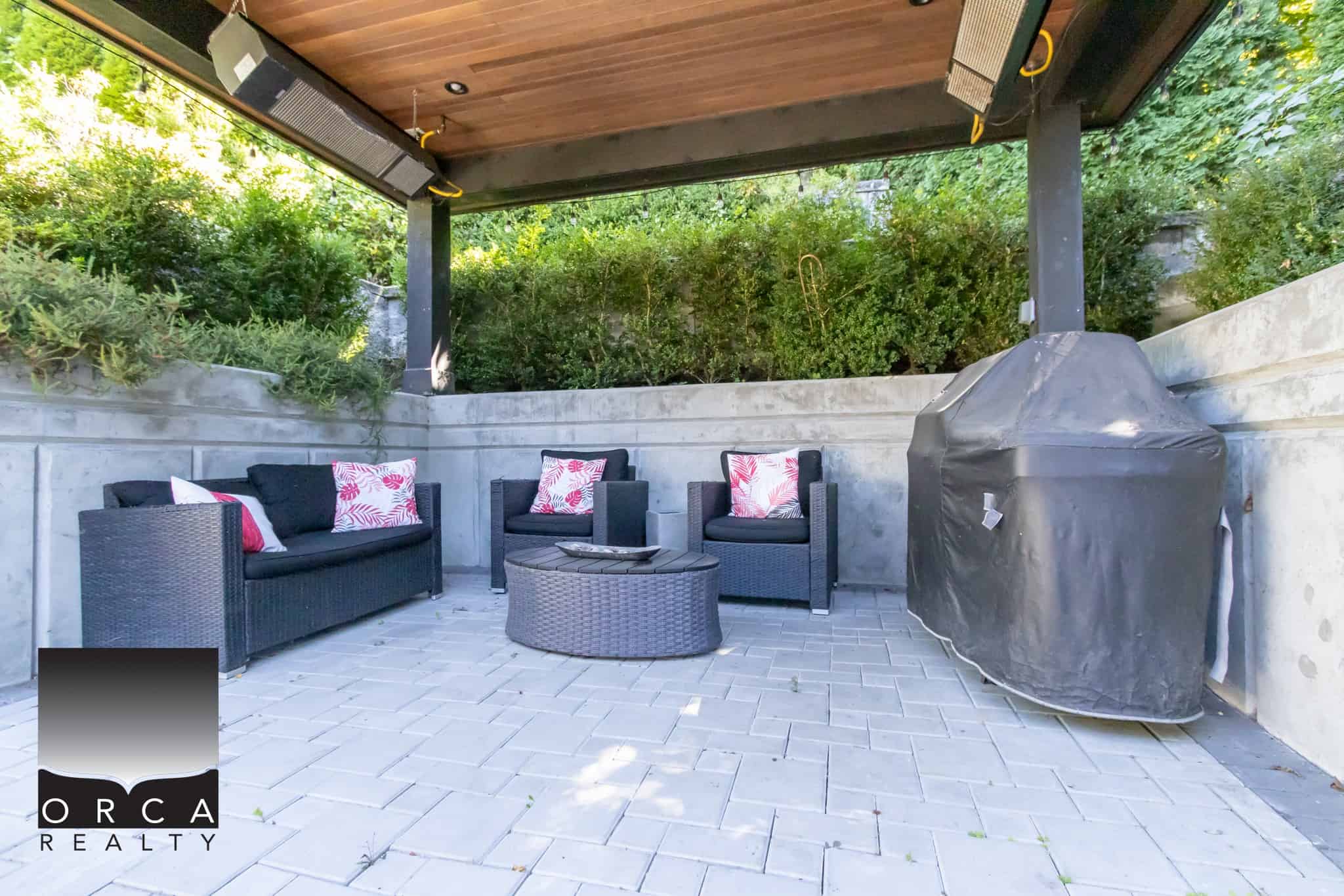 Cozy outdoor patio area with black wicker furniture, decorative pillows, and a covered BBQ grill, ideal for outdoor entertaining or relaxing in Vancouver’s real estate properties.