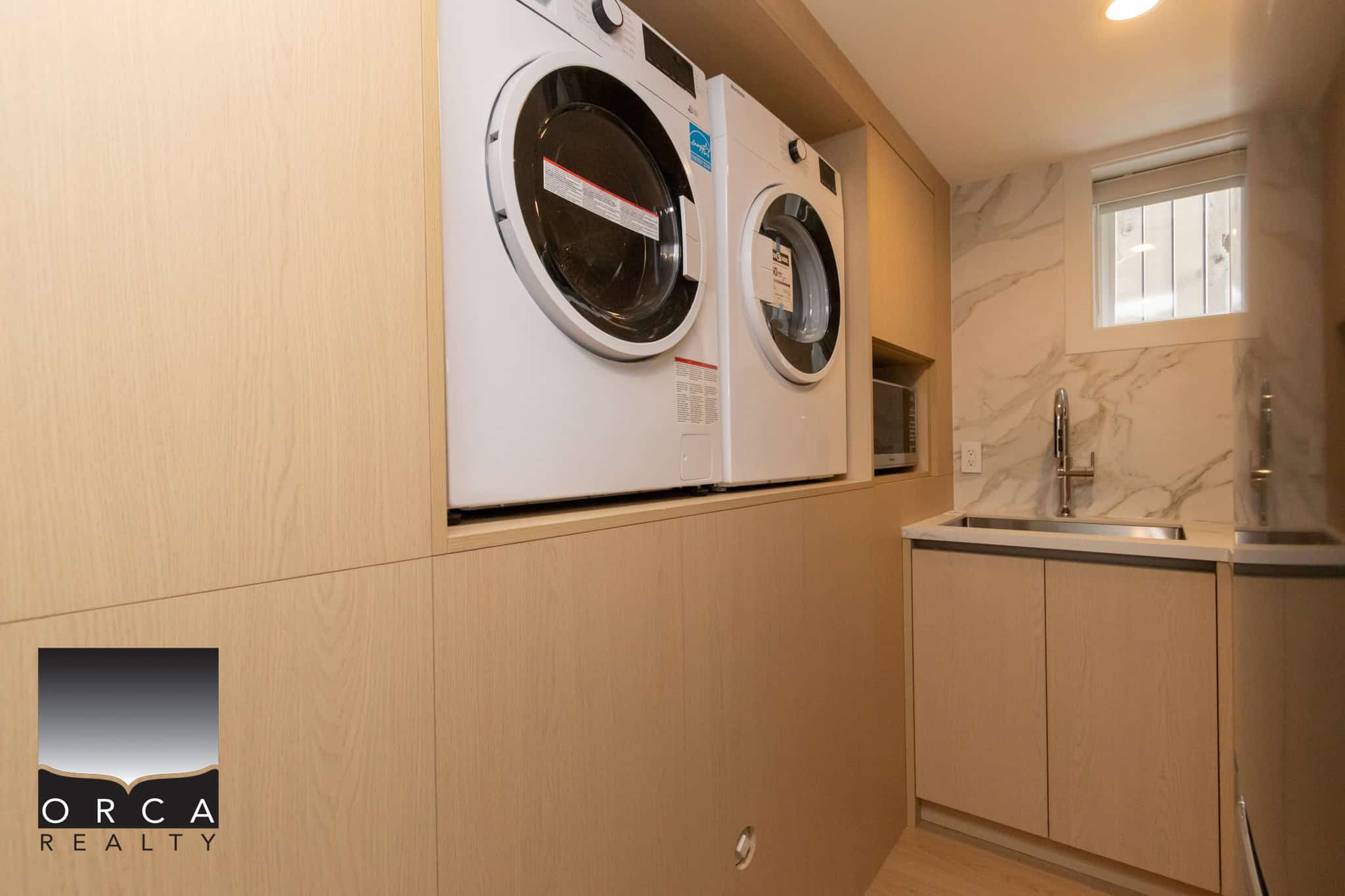 Modern laundry area with front-loading washer and dryer, built-in cabinetry, and a sleek countertop near a small window, ideal for efficient home organization and laundry routines.