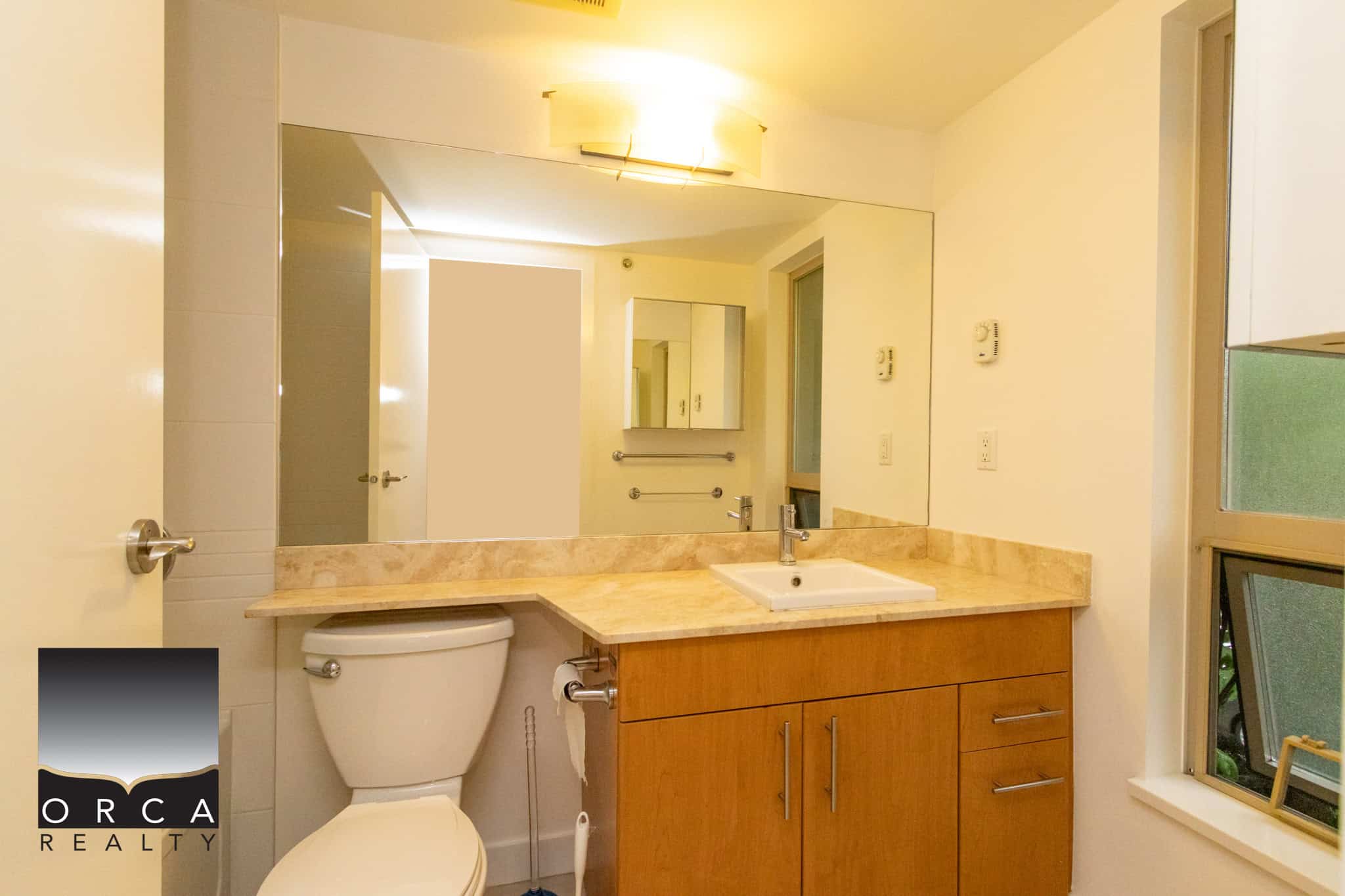 Bright modern bathroom with beige marble countertop, wooden vanity, and large mirror, featuring essential fixtures and a cozy window for natural light, ideal for Ontario homes.