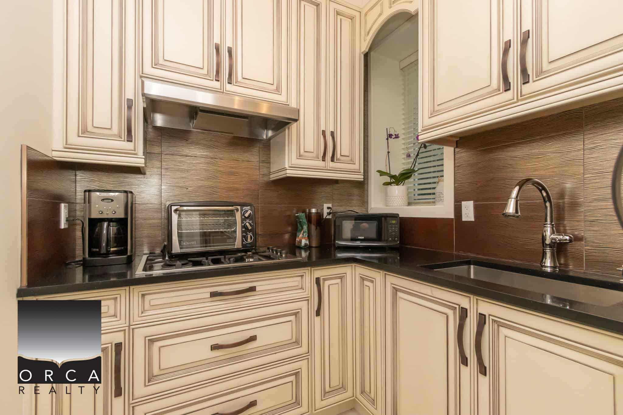 Cozy modern kitchen with cream cabinetry, black countertops, stainless steel appliances, and a decorative backsplash, perfect for Vancouver real estate listings.