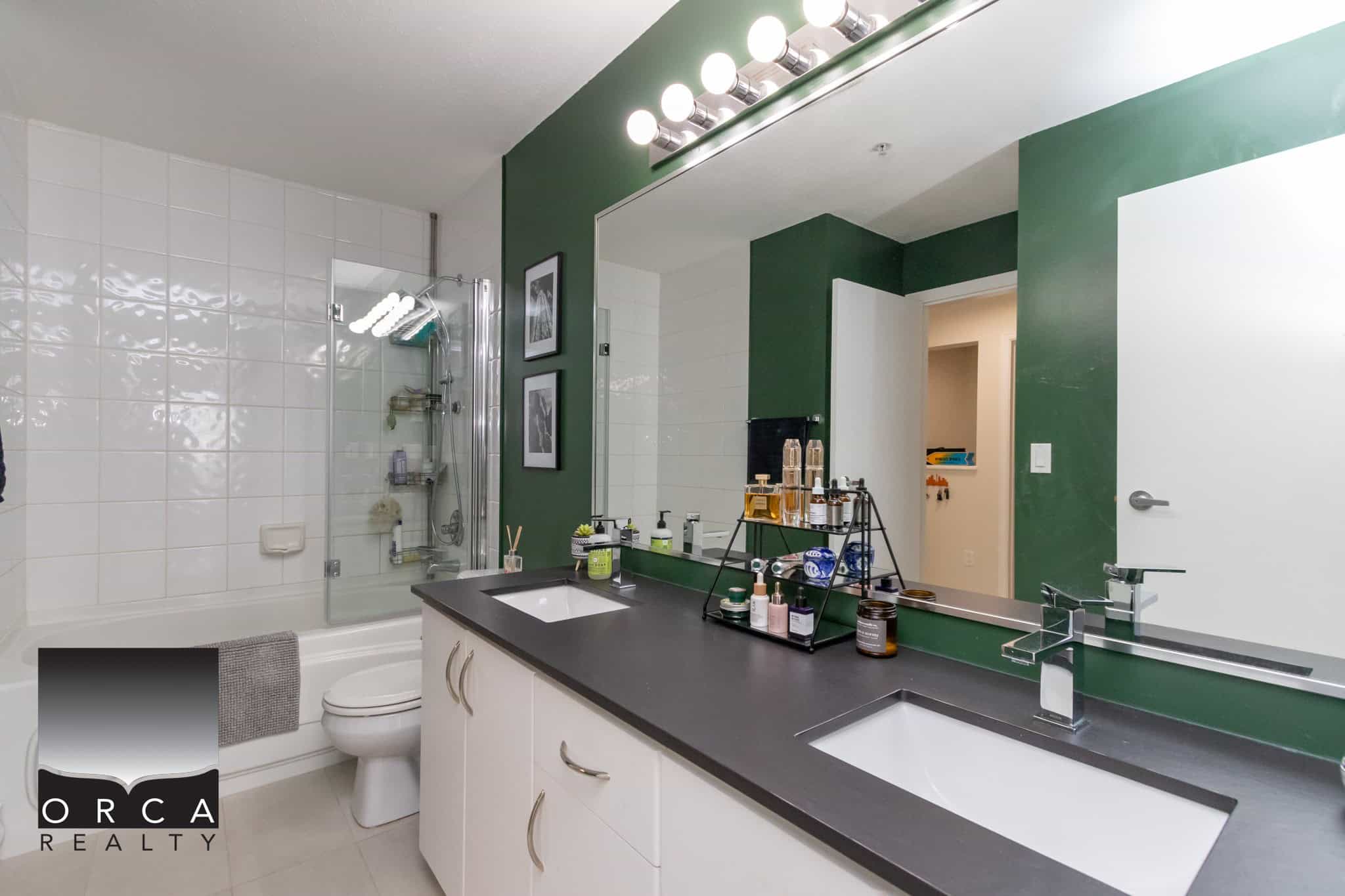 Bright modern bathroom featuring a double sink vanity, large mirror, green accent wall, and walk-in shower with glass doors, highlighting contemporary interior design.