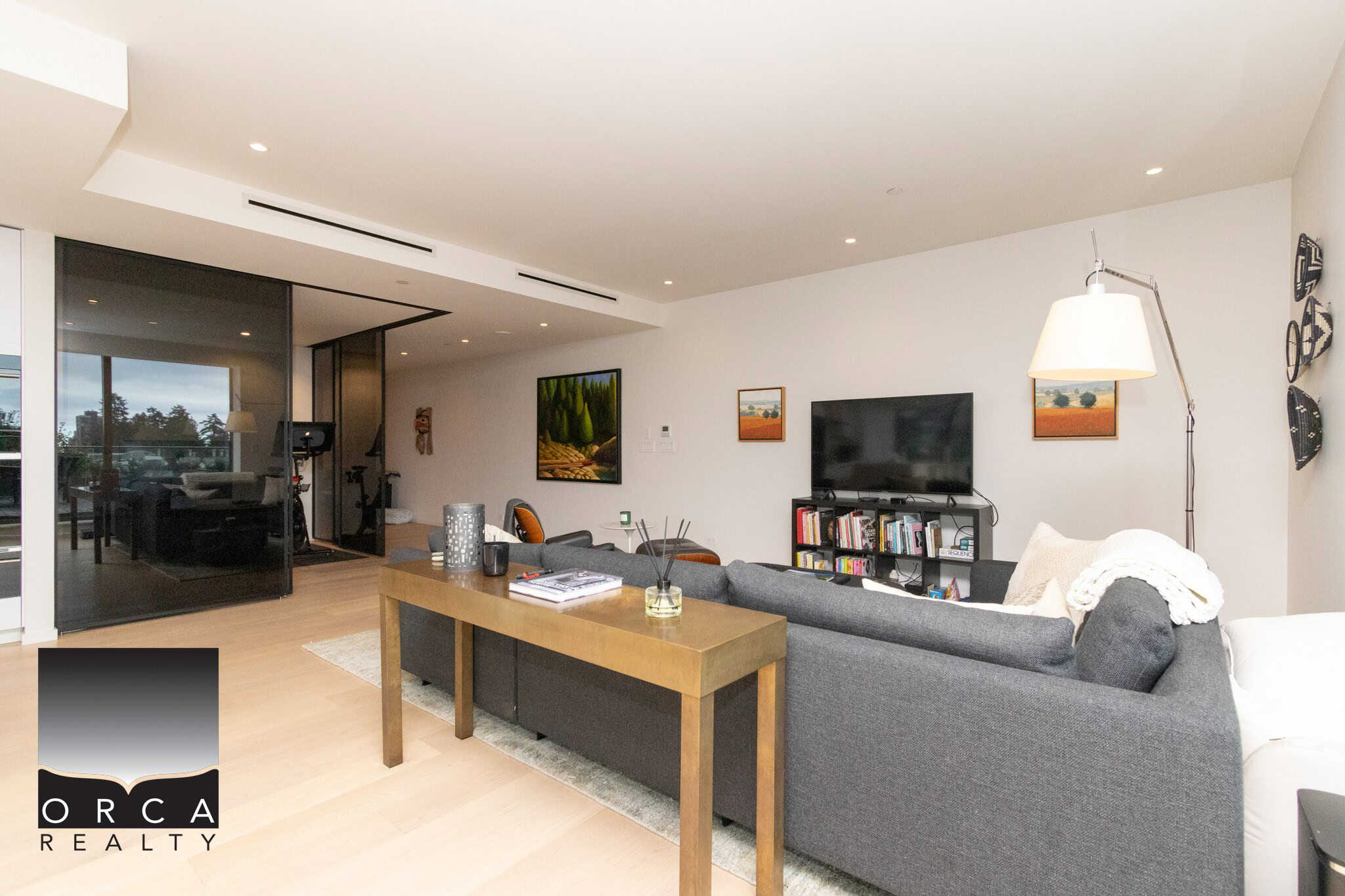 Modern living room interior with minimalist decor, grey sofa, wall-mounted TV, and artwork, showcasing upscale residential real estate in Canada by Orca Realty Inc.