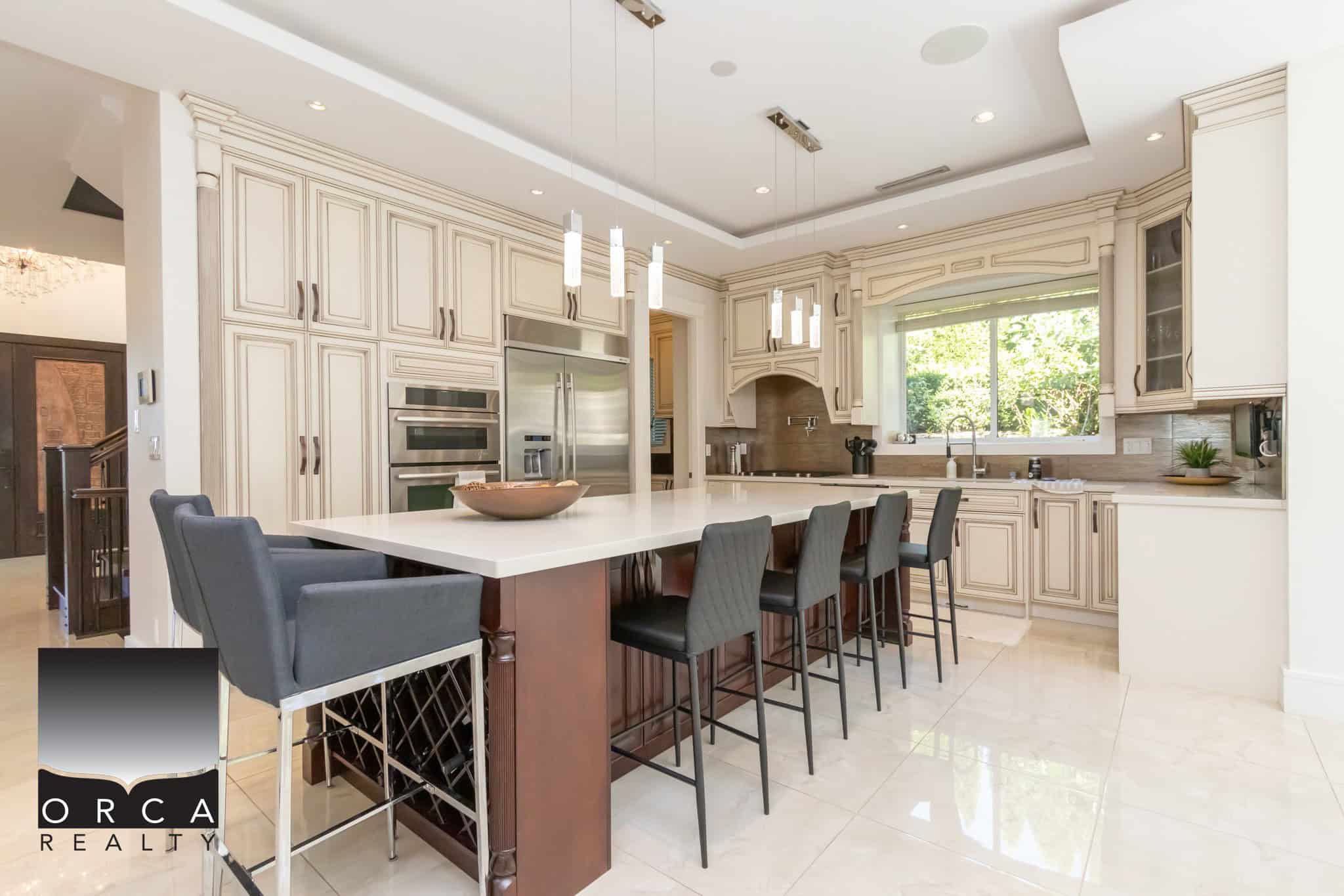 Modern kitchen with cream cabinetry, stainless steel appliances, large island, and ample natural light, perfect for luxury home living in Greater Vancouver area.