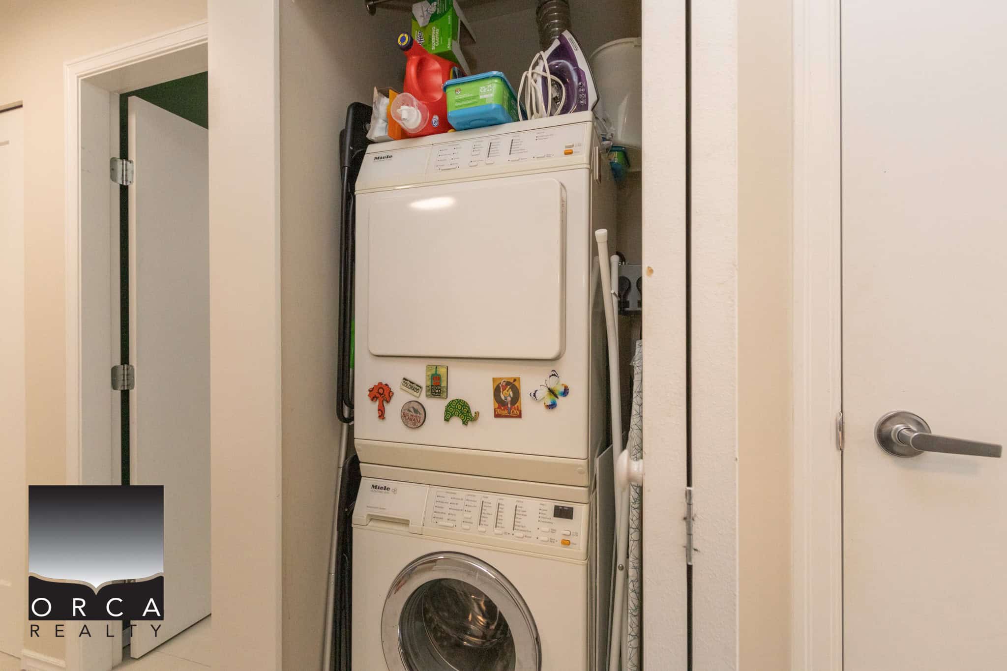 Stacked washer and dryer in a laundry closet with cleaning supplies and magnets on the appliances, showcasing a modern, functional laundry area in a Toronto home.
