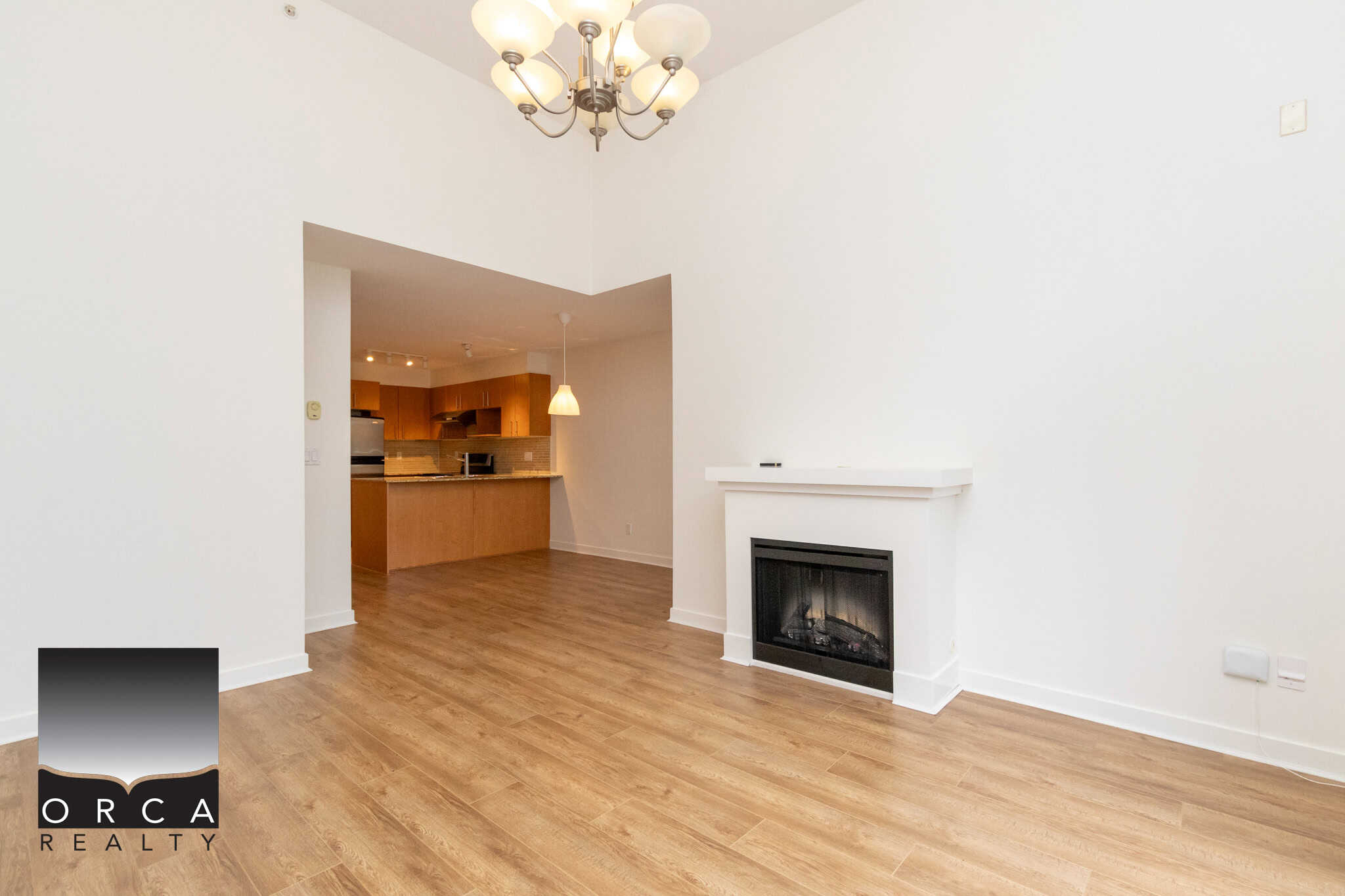 Modern living room with warm hardwood flooring, white walls, and a cozy fireplace, seamlessly connected to a stylish kitchen with wooden cabinetry and a breakfast bar, ideal for Vancouver Island real estate.