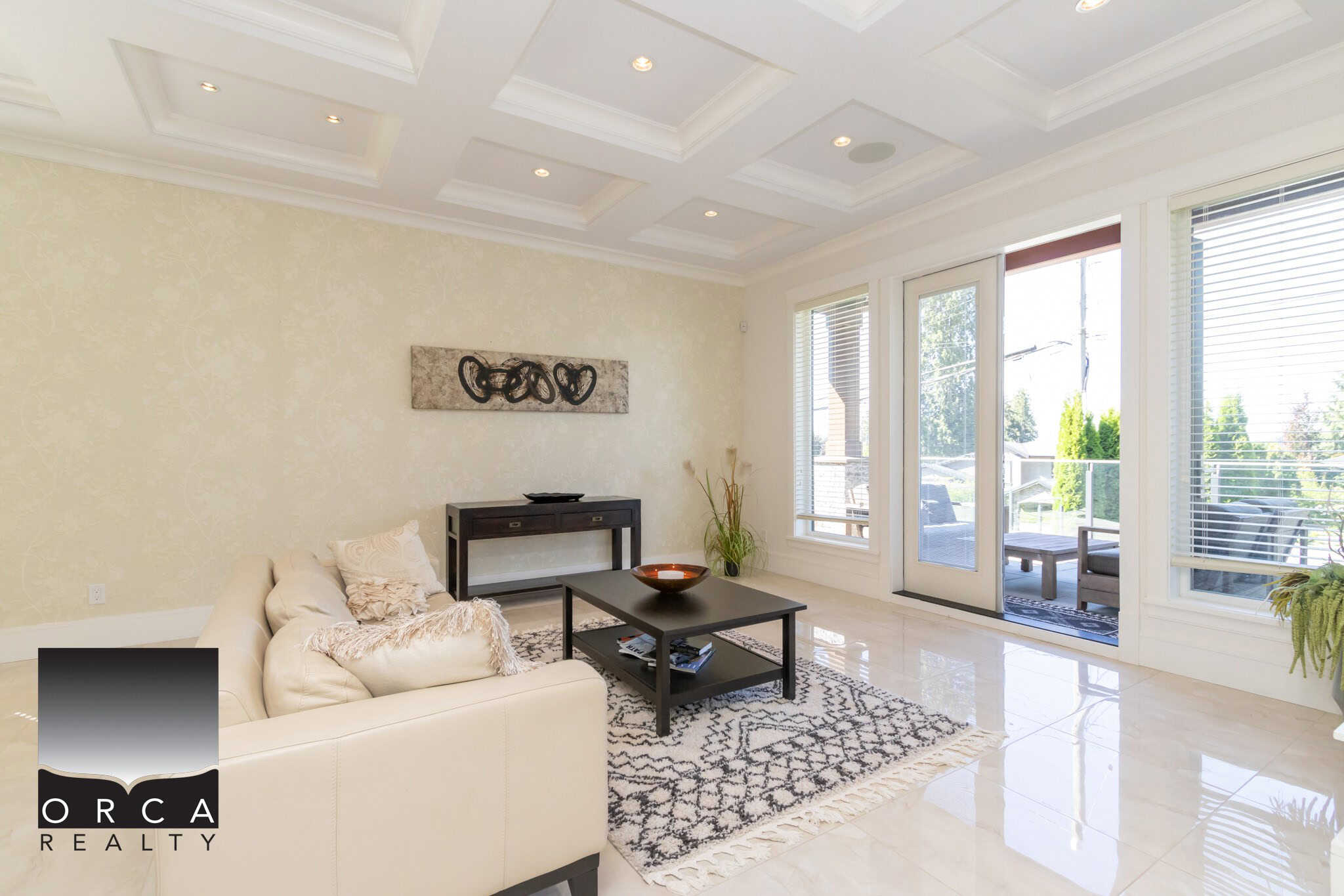 Bright living room with large windows, sliding glass door to outdoor patio, modern decor, cream sectional sofa, black coffee table, and natural light, perfect for Vancouver real estate opportunities.