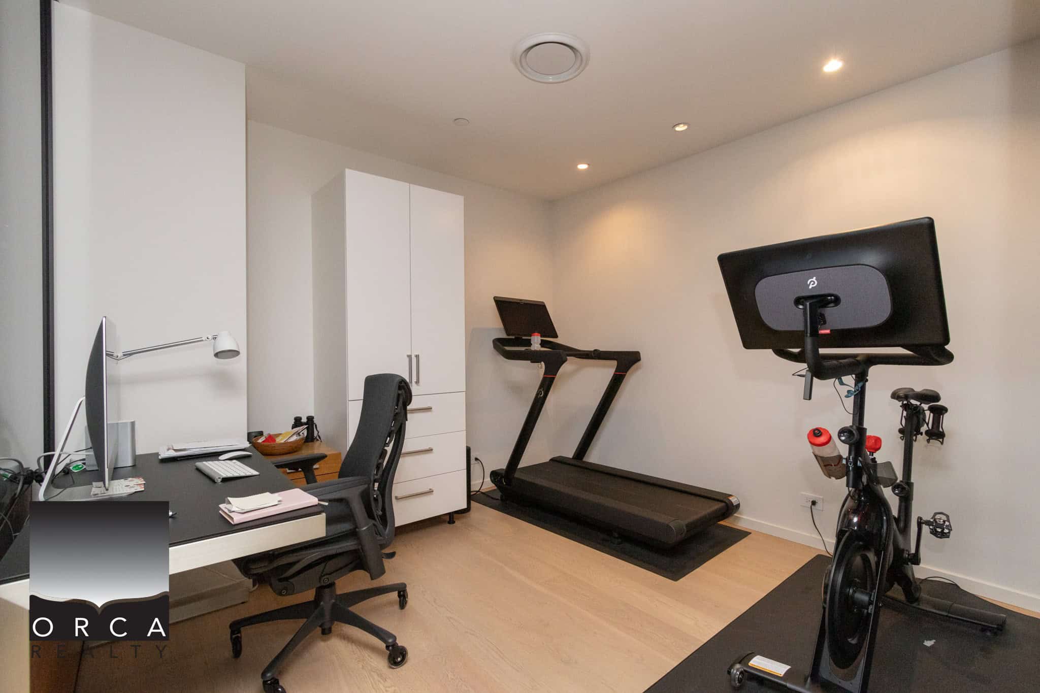 Modern home gym with treadmill and exercise bike, bright workspace with desk, chair, and white storage cabinets, perfect for active lifestyles, located in a beautiful California residence.