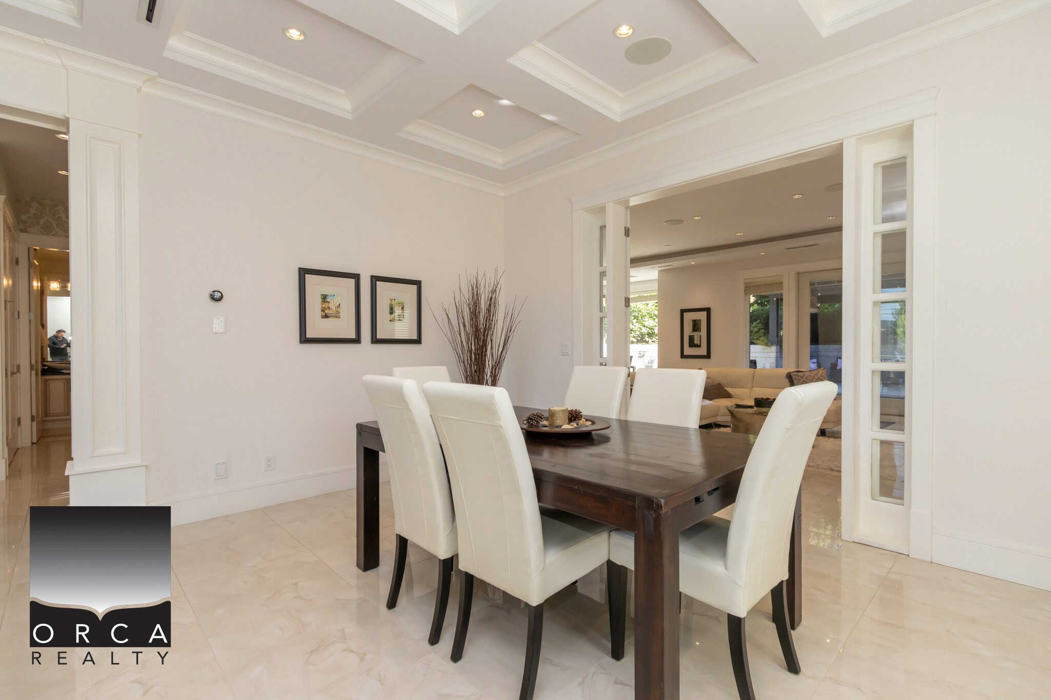 Modern dining room with elegant white walls, coffered ceiling, and large windows offering natural light; ideal for luxury home living and showcasing Orca Realty Inc. services in real estate.