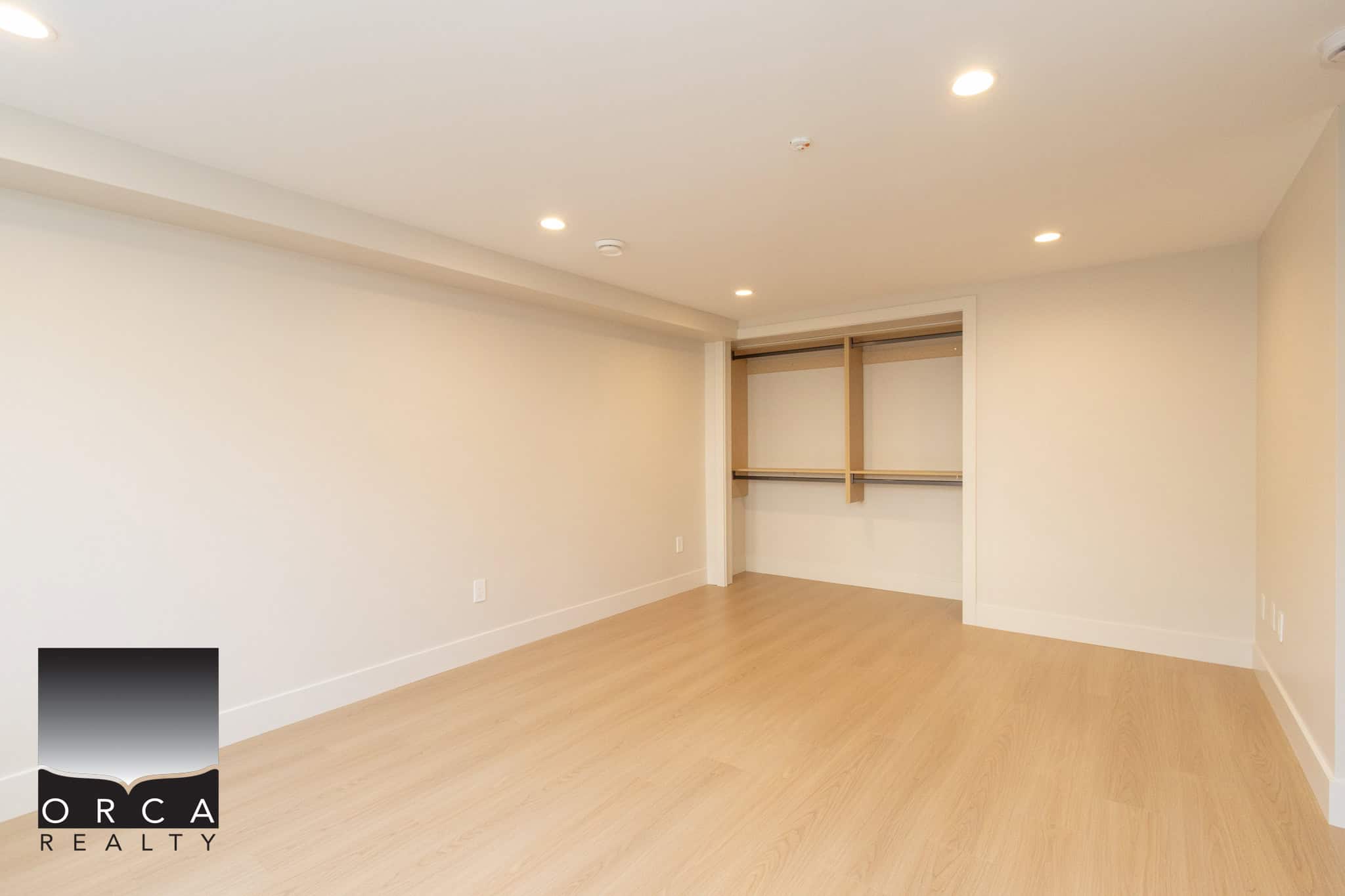 Bright, spacious empty bedroom with walk-in closet, modern recessed lighting, and light wood flooring in a contemporary home listing by Orca Realty Inc.