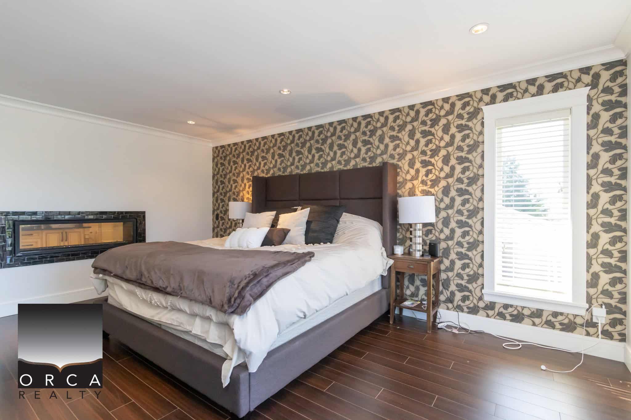 Stylish modern bedroom with a large bed, decorative wallpaper accent wall, and contemporary furniture, showcasing Orca Realty Inc.’s expertise in Vancouver Island real estate.
