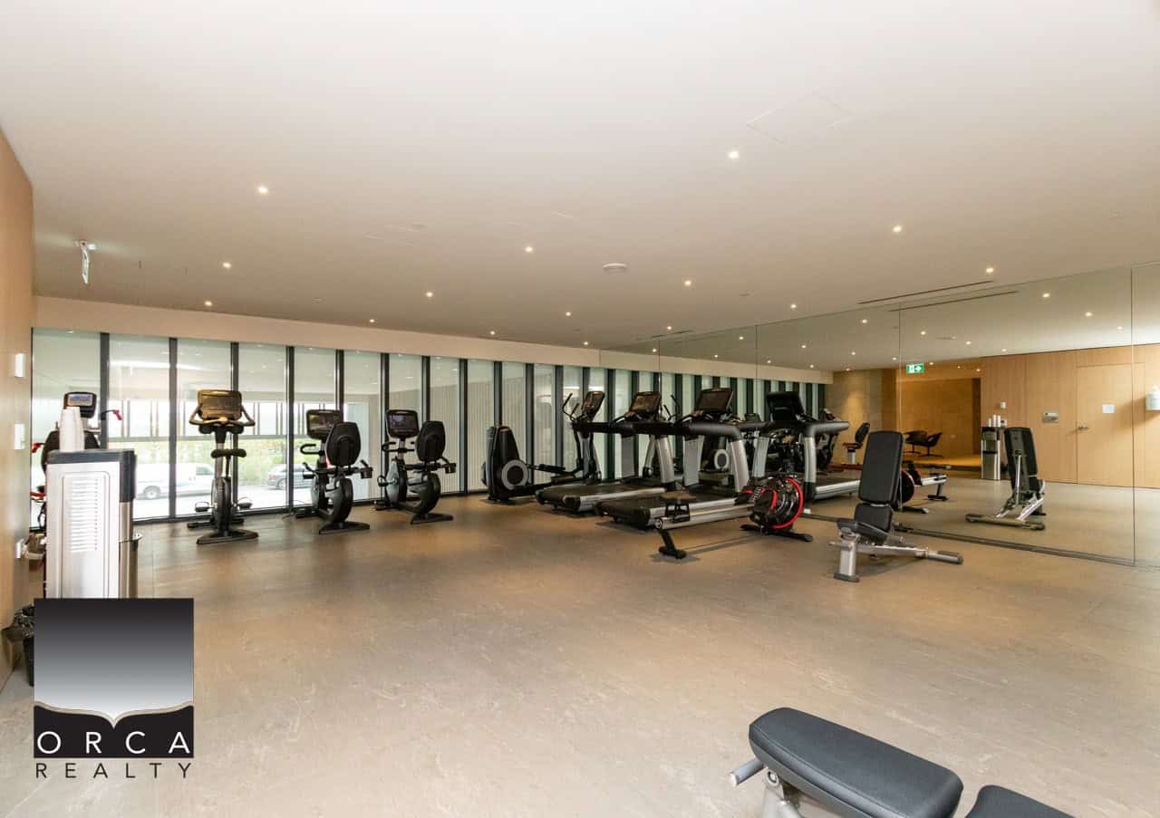 Modern fitness centre with cardio and strength equipment at Orca Realty Inc. Vancouver Island property. State-of-the-art gym amenities for residents in a luxury real estate setting.