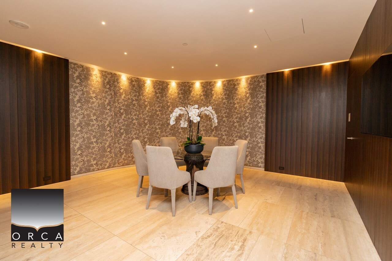 Modern dining area with elegant cream chairs, floral wallpaper, and ambient lighting, showcasing luxury real estate features by Orca Realty Inc.