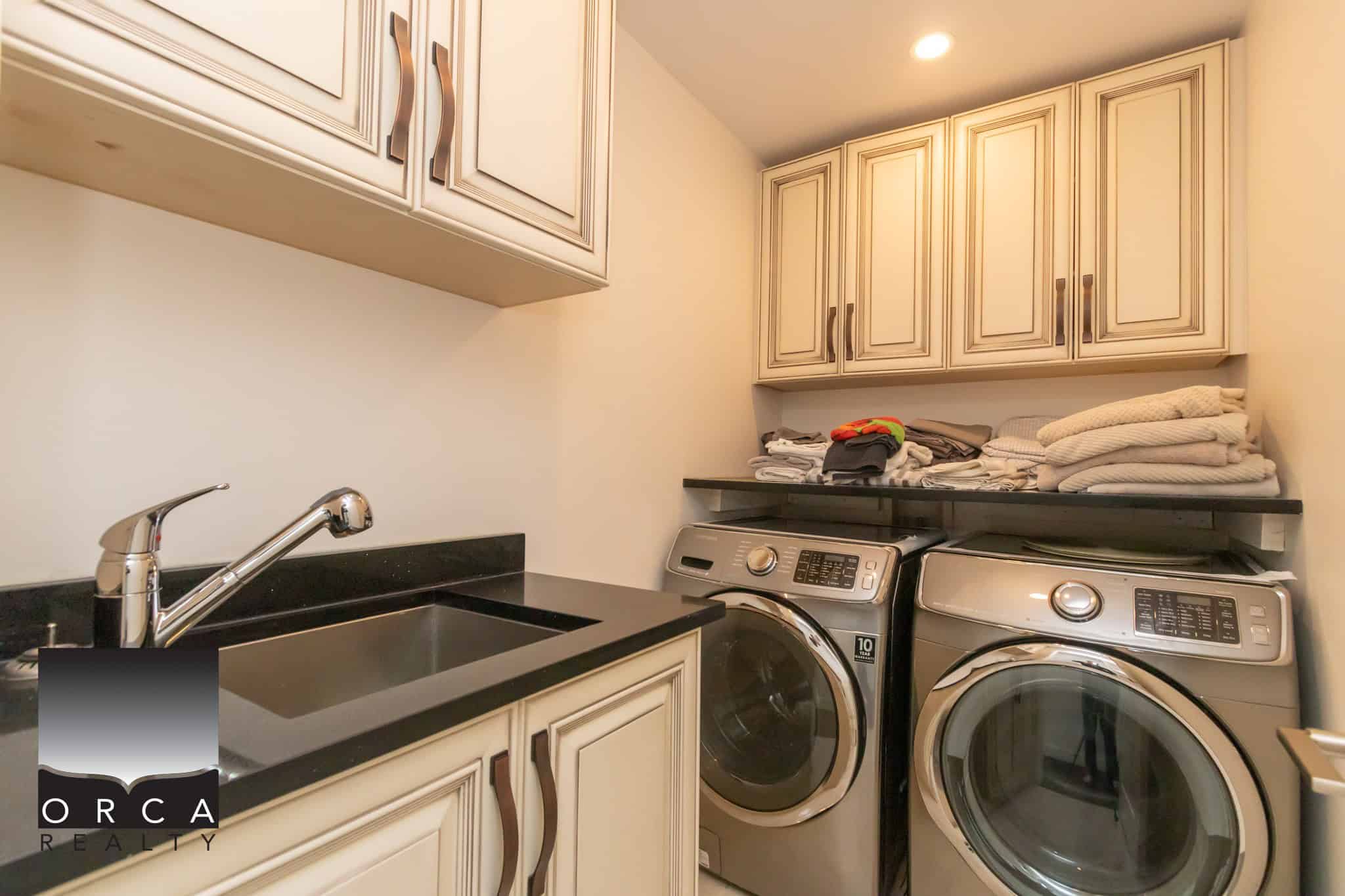 Clean laundry room with washer and dryer, beige cabinetry, black countertop, and stacked shelves for storage - ideal for house resale.