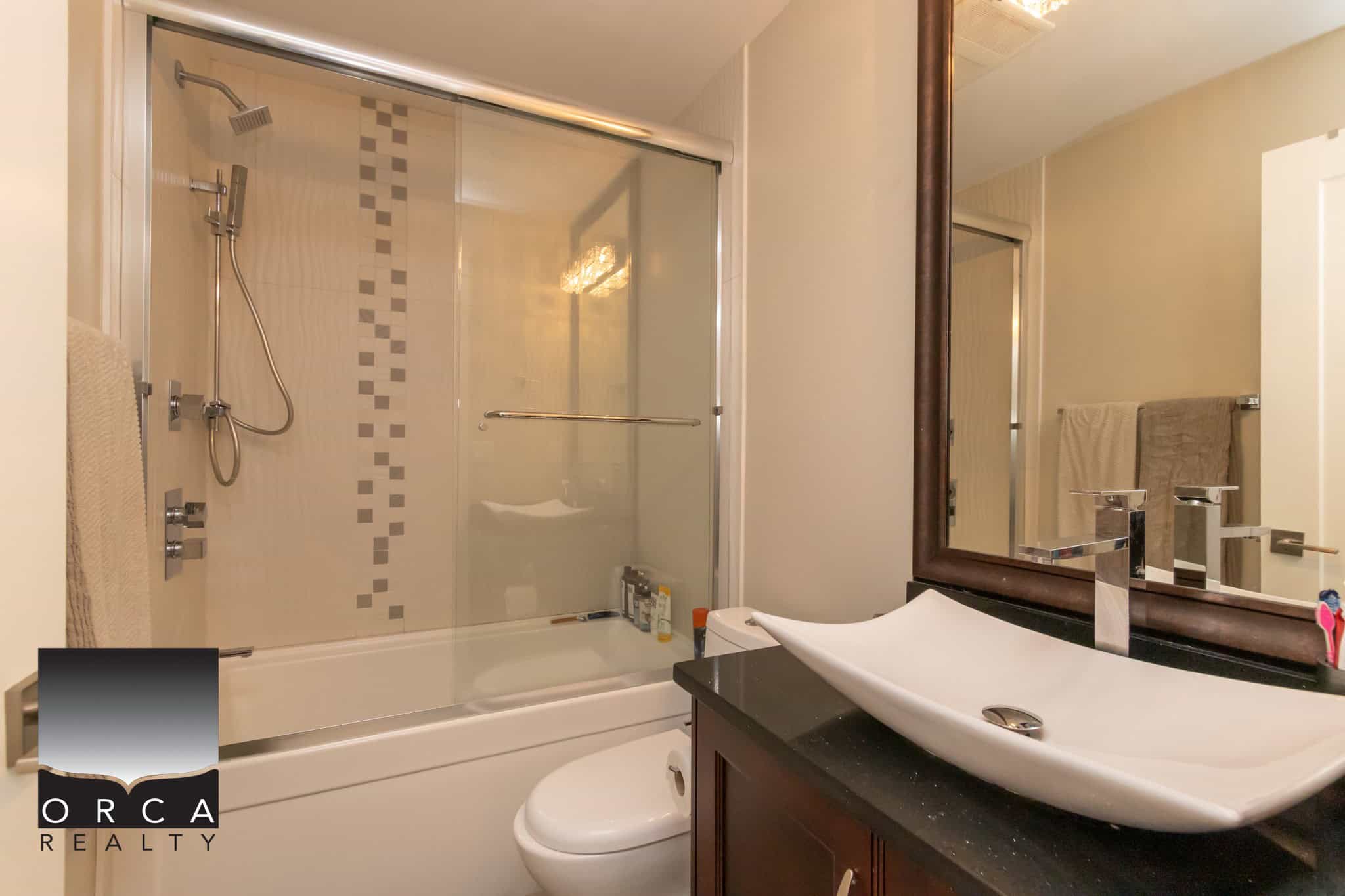 Modern bathroom with walk-in shower, stylish vanity with vessel sink, and contemporary fixtures in a well-maintained Orca Realty property.