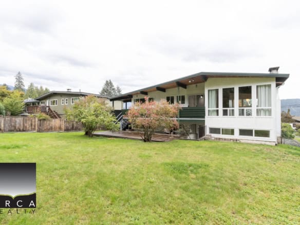 Spacious backyard of a modern residential property with lush green lawn, mature trees, and a wooden fence, showcasing the inviting outdoor space available through Orca Realty Inc.