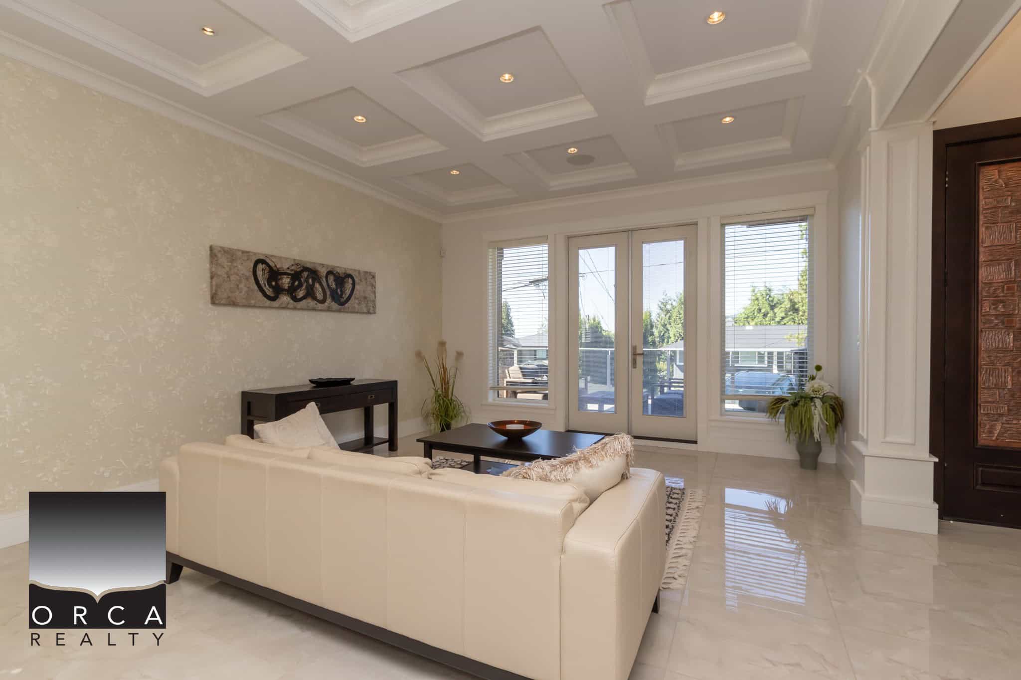 Spacious modern living room with large windows, luxurious cream-colored sofa, elegant ceiling design, and stylish decor, perfect for showcasing Vancouver Island homes and real estate.