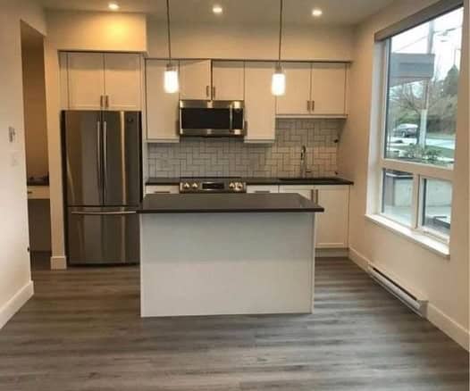 Modern kitchen with stainless steel appliances, white cabinetry, and a central island in a bright, open space with large windows and laminate flooring.
