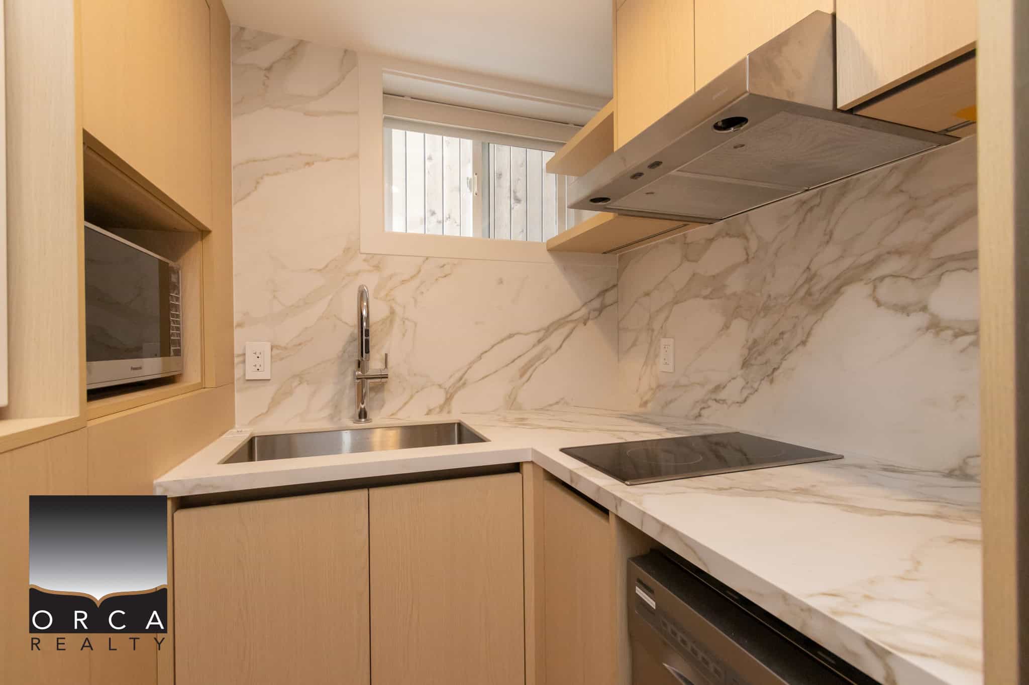 Sleek modern kitchen with marble countertops, built-in microwave, and minimalist cabinetry, showcasing luxury condo features in Vancouver by Orca Realty Inc.