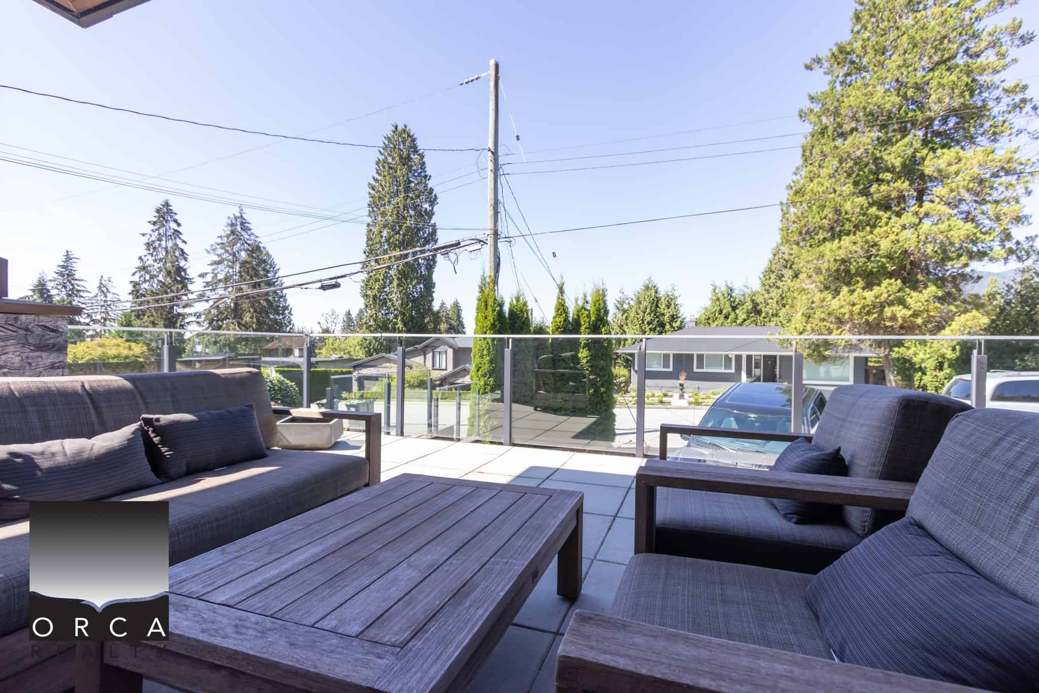 Modern outdoor patio with glass railing, comfortable seating, and lush green trees, perfect for relaxing or entertaining in a scenic residential setting in Vancouver.
