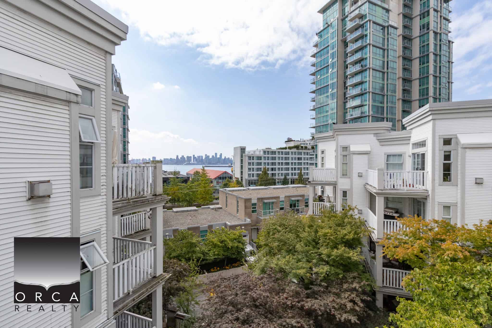 Vibrant cityscape view from a modern apartment balcony in downtown Vancouver, BC, featuring high-rise buildings, lush trees, and a distant skyline, perfect for Vancouver real estate and urban living.