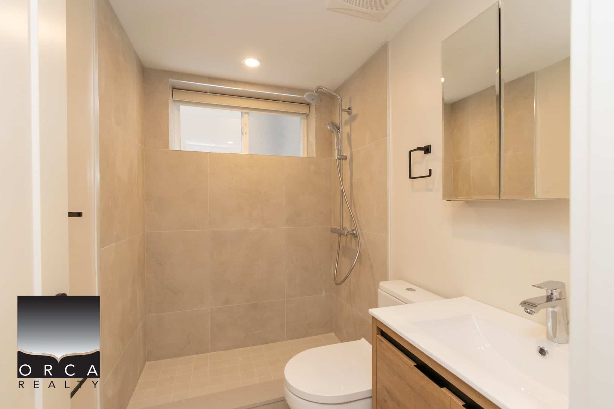 Bright modern bathroom with beige tiles, walk-in shower with rain showerhead, contemporary vanity with sink and mirror, ideal for Vancouver real estate listings.