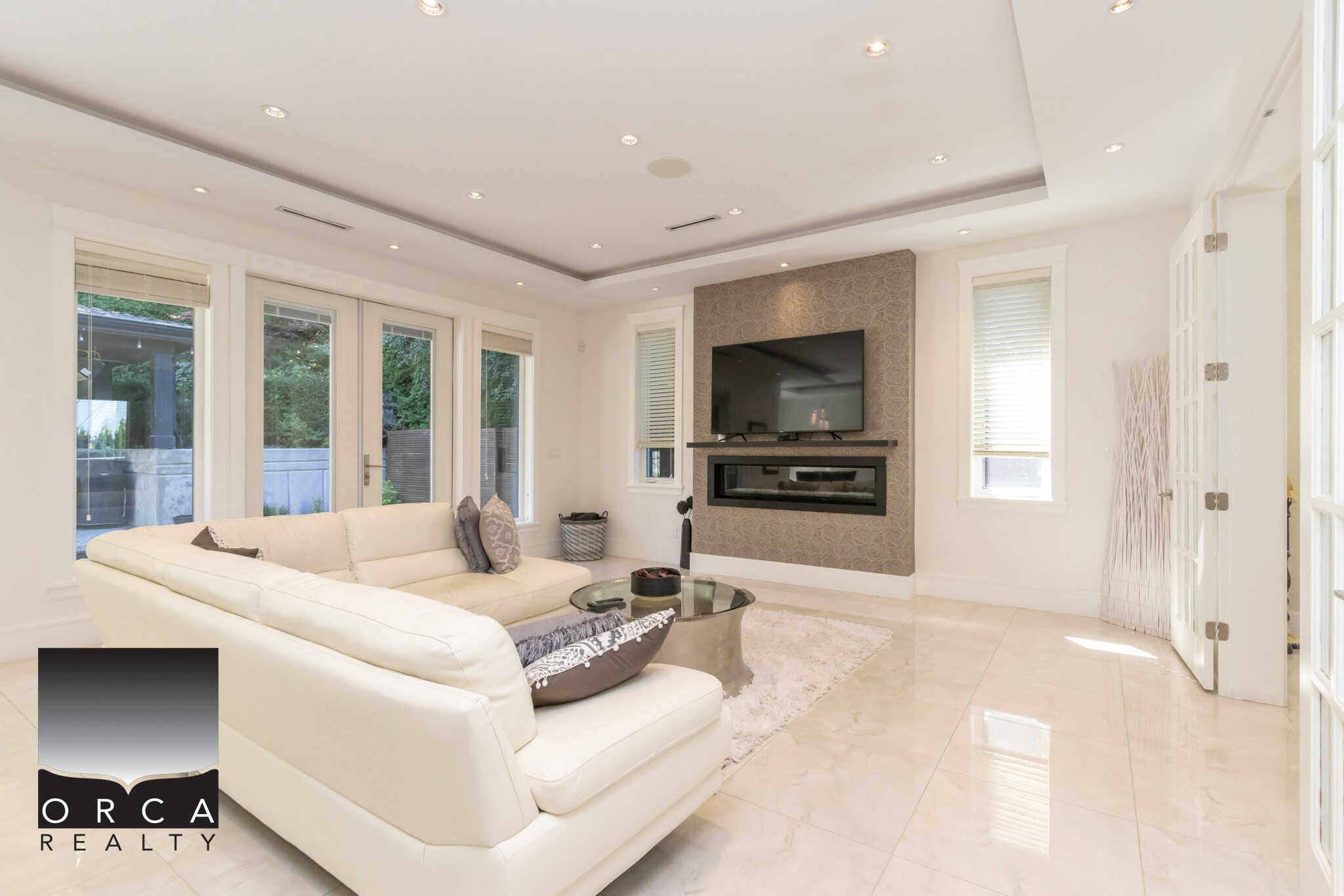 Modern living room featuring a cozy white sectional sofa, large windows with natural light, and a sleek wall-mounted TV, perfect for Vancouver Island real estate buyers.