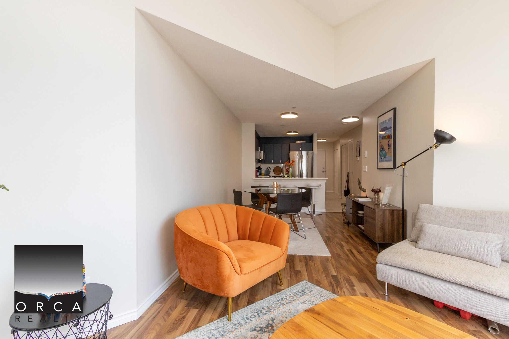 Bright, modern living room with stylish orange and beige seating, open floor plan, hardwood floors, and contemporary decor in Vancouver condo, offered by Orca Realty Inc.