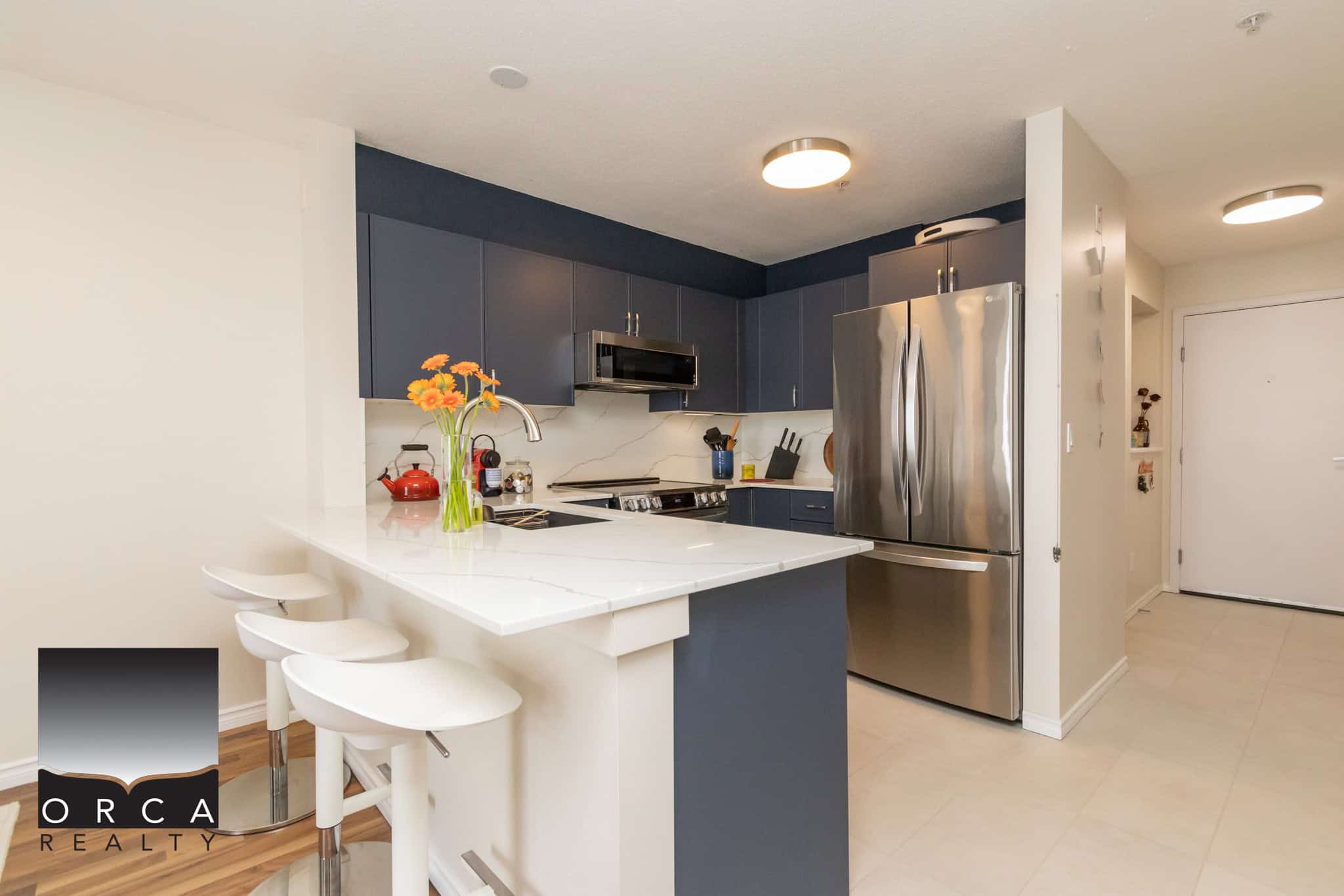 Modern kitchen with stainless steel appliances, navy blue cabinets, white countertops, and casual seating area, ideal for comfortable urban living.