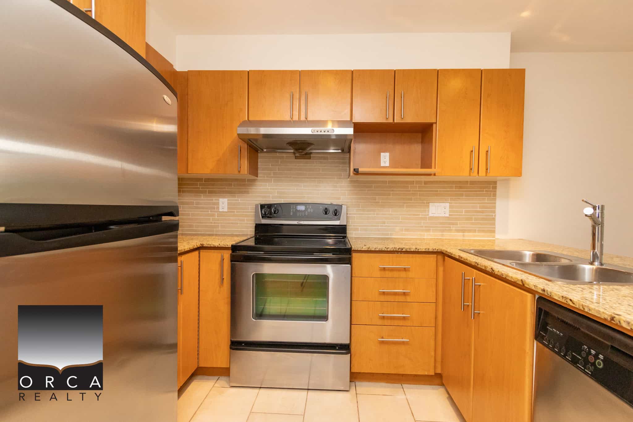 Modern kitchen with stainless steel appliances, wooden cabinets, granite countertops, and a tile backsplash, ideal for Vancouver Island real estate buyers seeking stylish and functional homes.