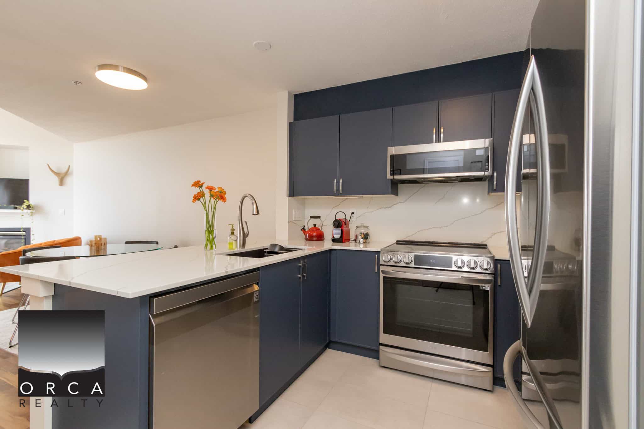 Modern kitchen with navy blue cabinets, stainless steel appliances including a refrigerator, oven, and microwave, quartz countertop, and stylish backsplash. Perfect for Vancouver real estate listings and homebuyers.
