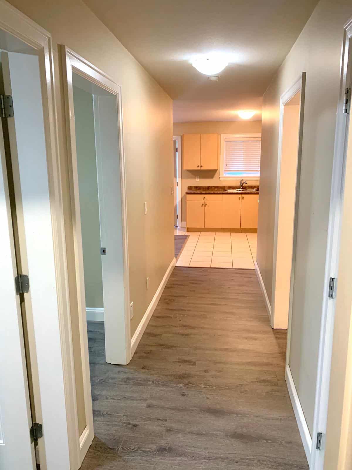 Bright kitchen and hallway in a modern home with laminate flooring and neutral wall colours, featuring a spacious kitchen with wooden cabinets and a large window.