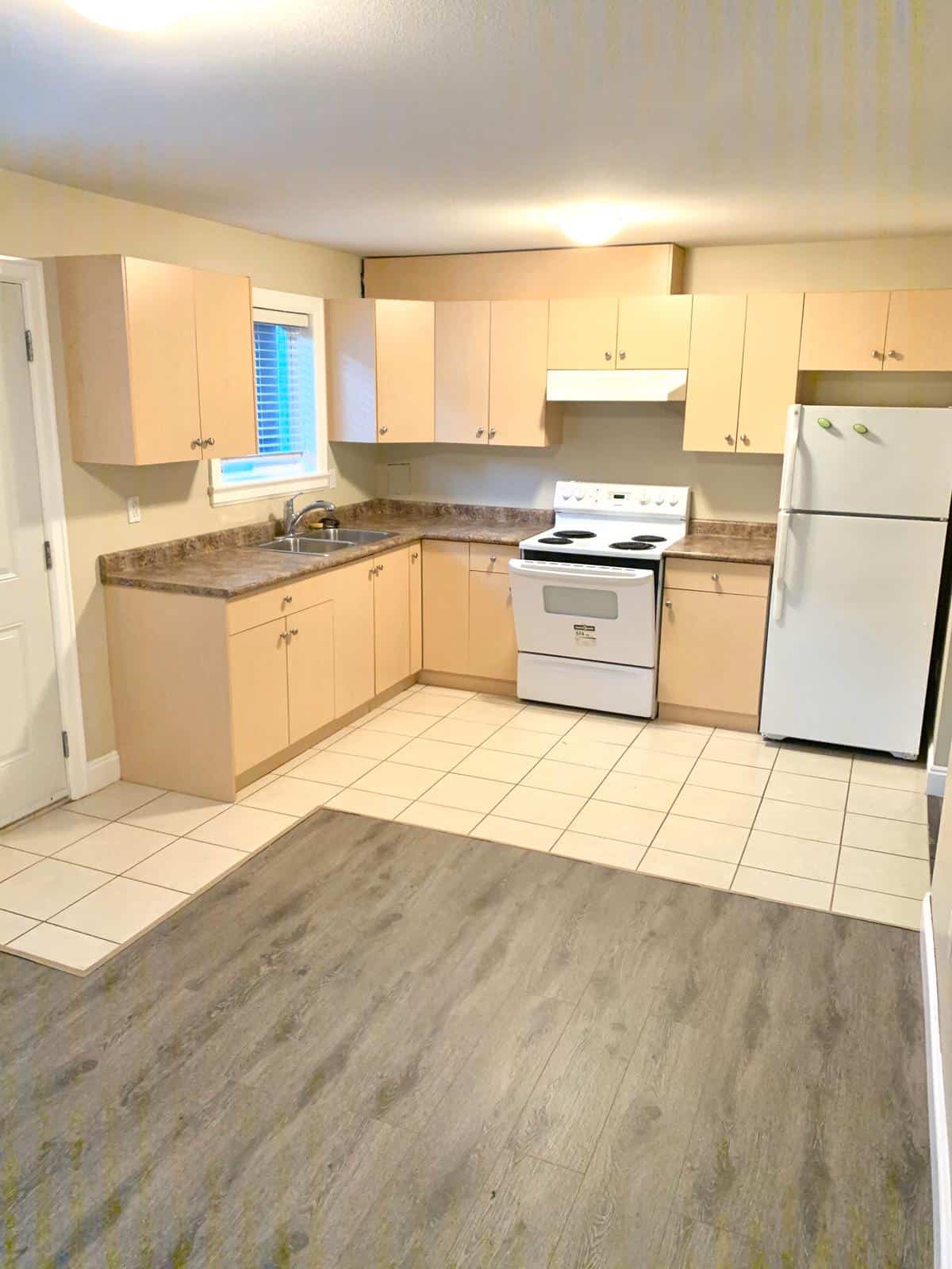 Bright kitchen with beige cabinets, white appliances, and a window overlooking the yard, ideal for Vancouver Island real estate.