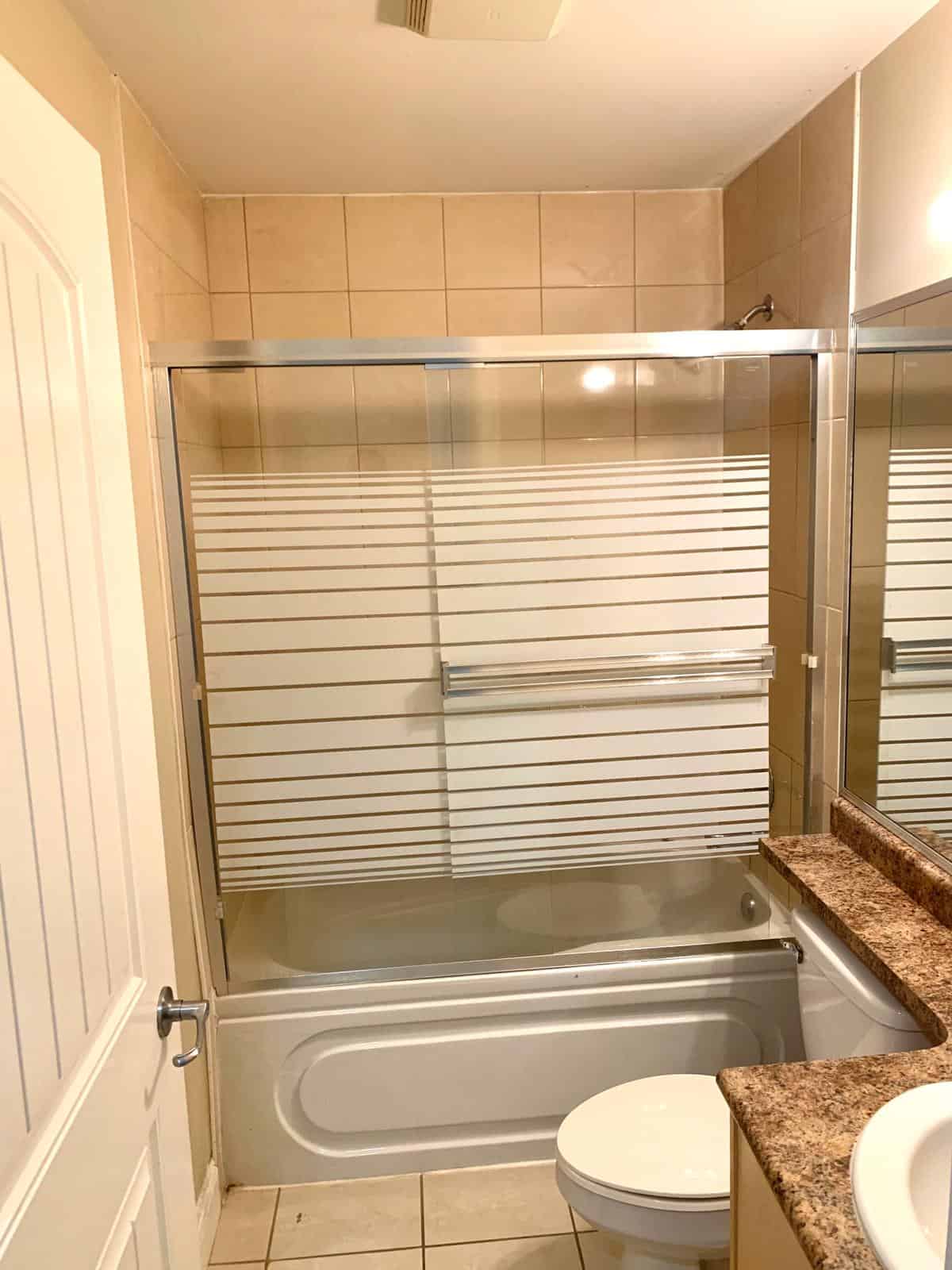 Modern bathroom with bathtub, glass shower enclosure, beige tiles, and granite countertop in a residential property. Ideal for condos or homes seeking contemporary design and comfort.