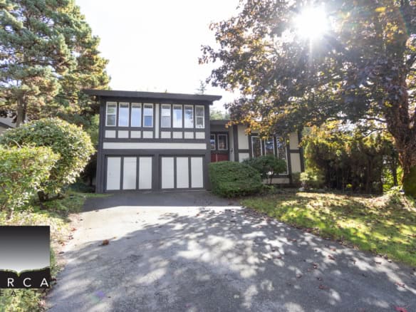 Charming Tudor-style house with a large driveway, lush greenery, and mature trees, perfect for those seeking residential real estate in a tranquil Vancouver neighbourhood.