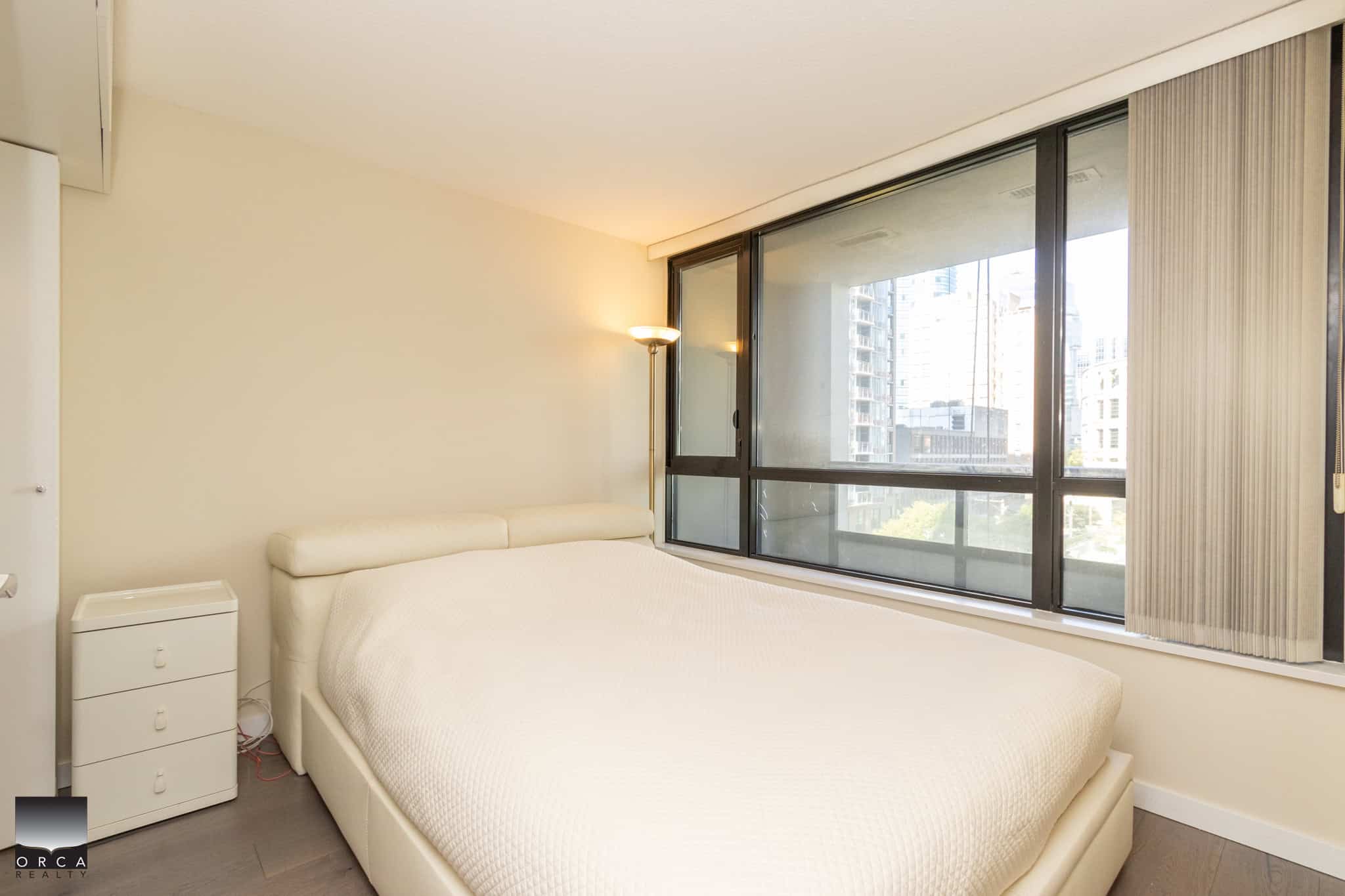Modern downtown Vancouver furnished bedroom with large windows, city views, minimalist decor, and natural light, ideal for condo living or urban real estate investment.
