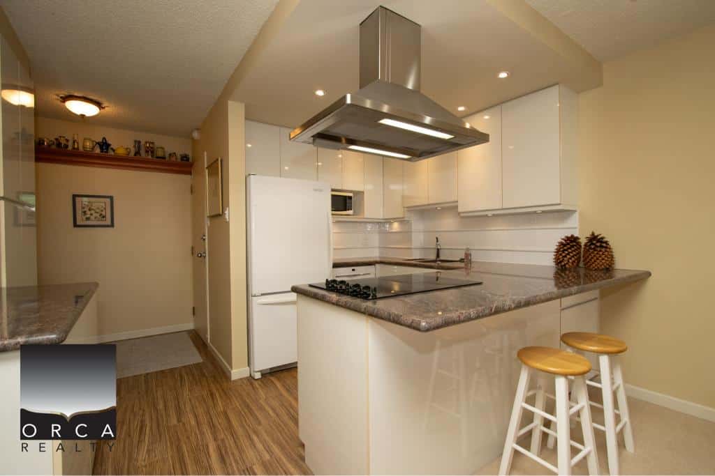 Bright modern kitchen with white cabinetry, granite countertops, stainless steel appliances, and a functional layout, perfect for Vancouver Island homes and real estate listings.